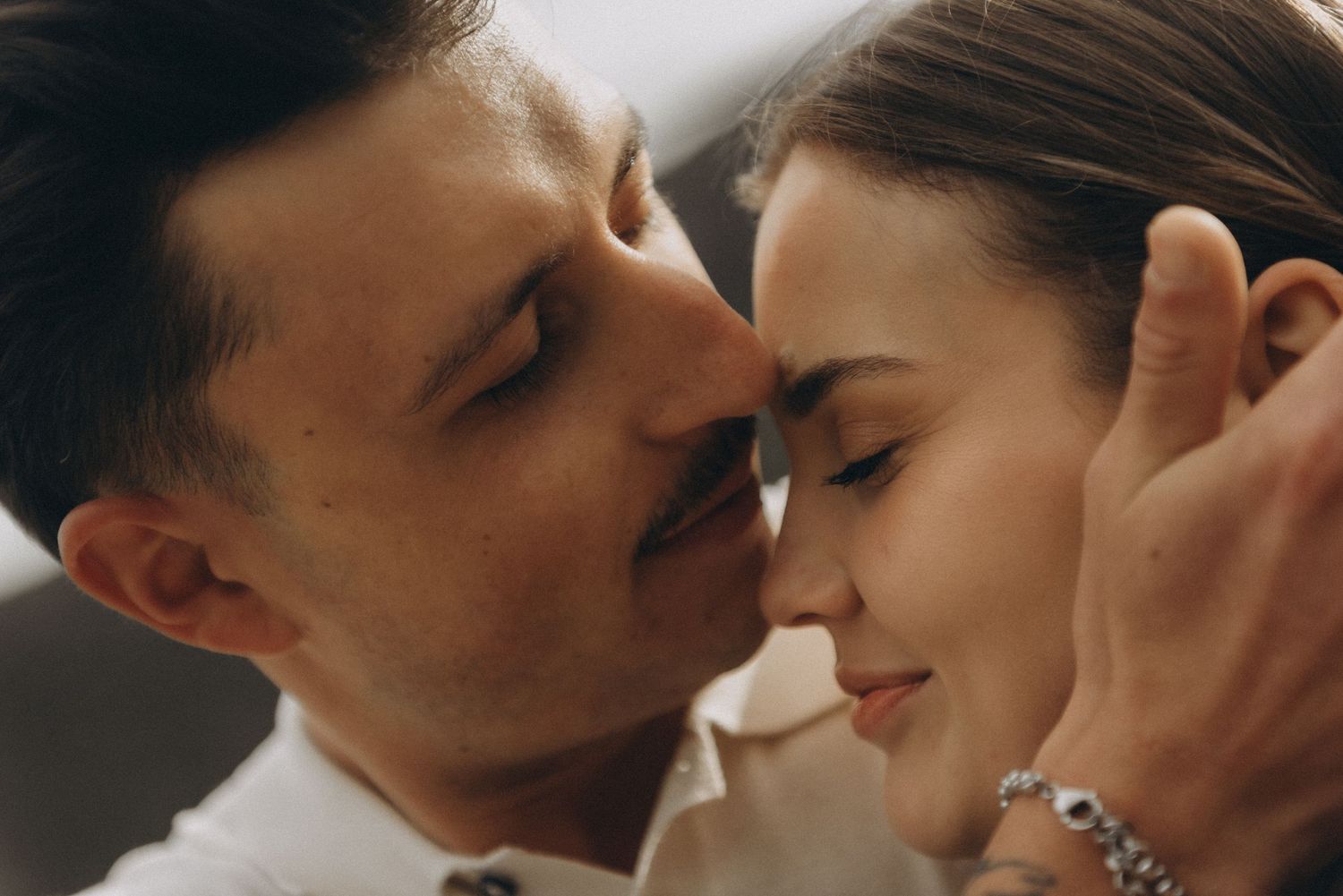 A romantic couple sharing an intimate moment, faces close together, man in white shirt, woman with bracelet.