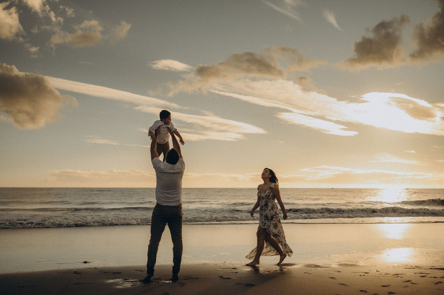 Silhouettes of people walking along a beach at sunset with dramatic golden clouds in the sky.