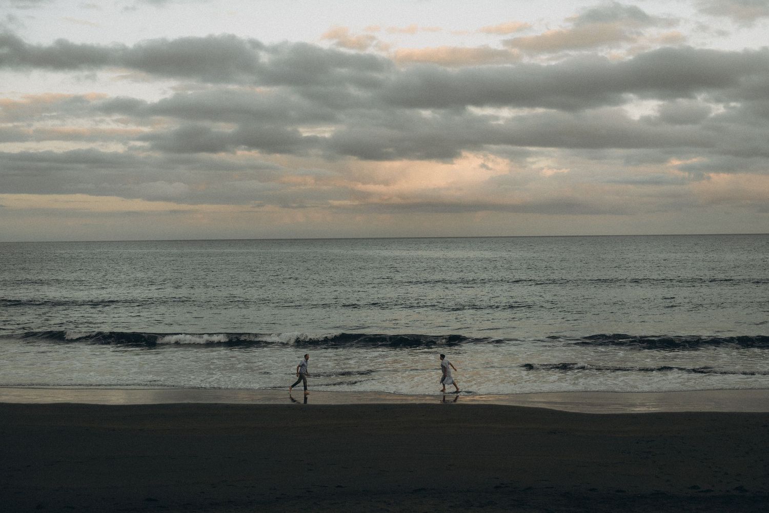 Two people jogging along a serene beach at dusk with cloudy skies and calm ocean waves in the background.