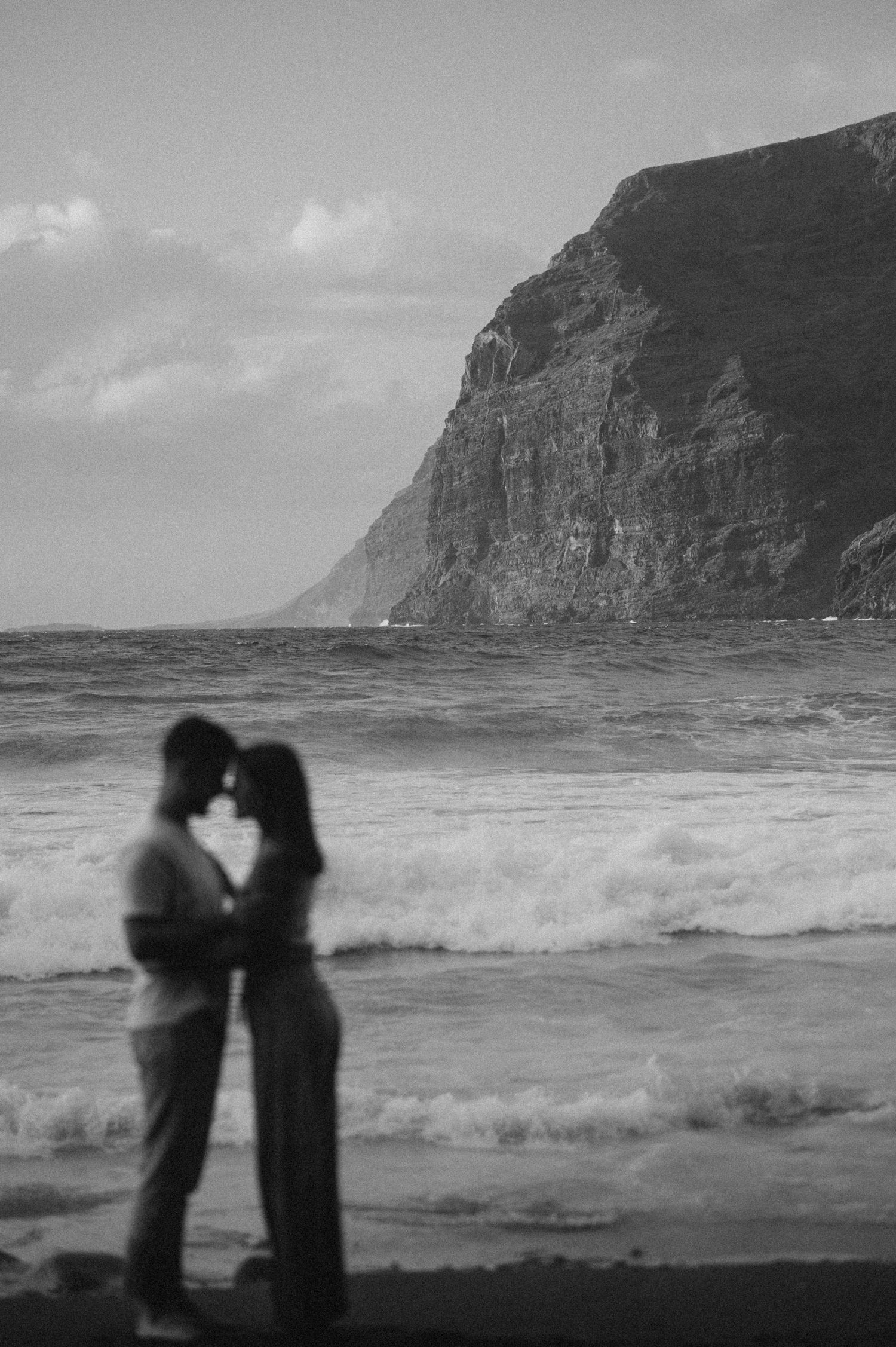 Romantic couple in distance on Playa de Los Guíos, Tenerife with ocean and dramatic cliffs