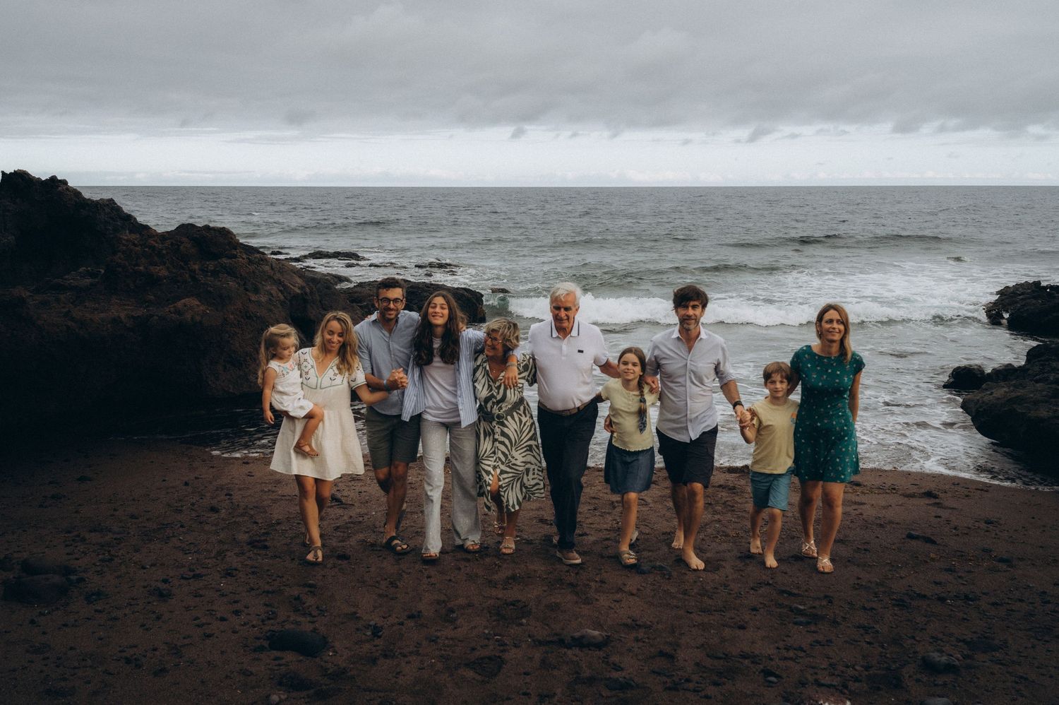 Three-generation family walking from Atlantic Ocean toward camera on black sand at Los Refugios, Tenerife