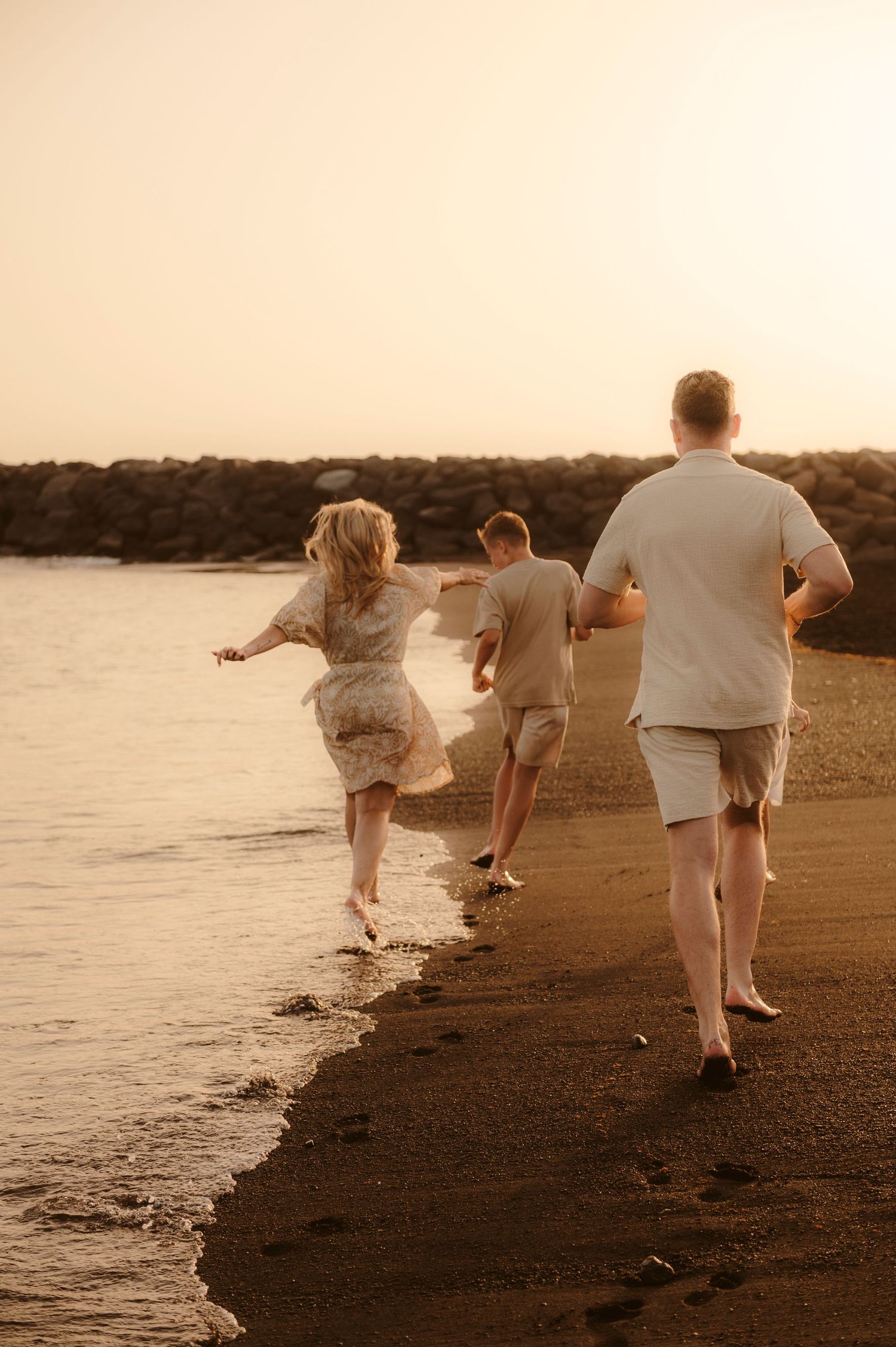 Family moment on volcanic sand with ocean foam and sunset in background, Tenerife