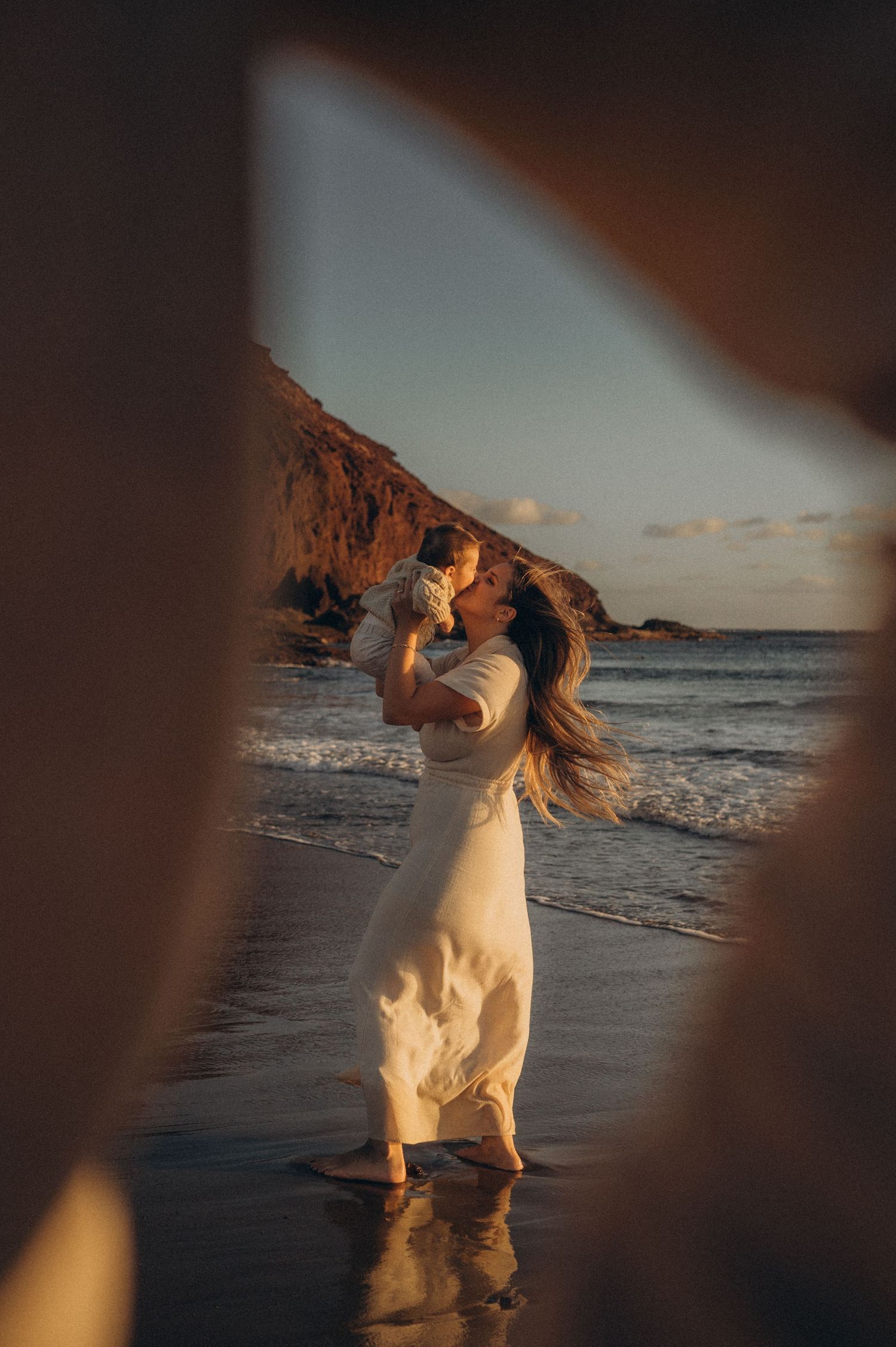 White dog running and playing on a beach at sunset with ocean waves in the background.