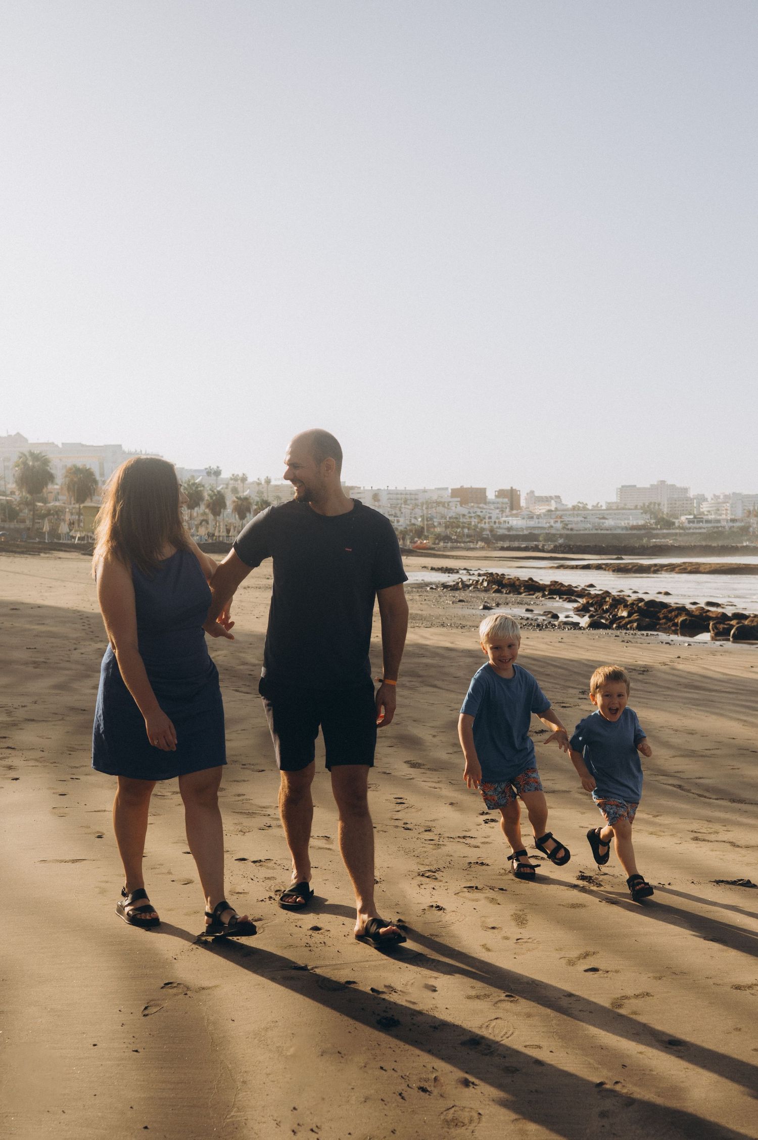 Tender morning moment of parents leading their sons along the sandy shore at Playa Fañabé