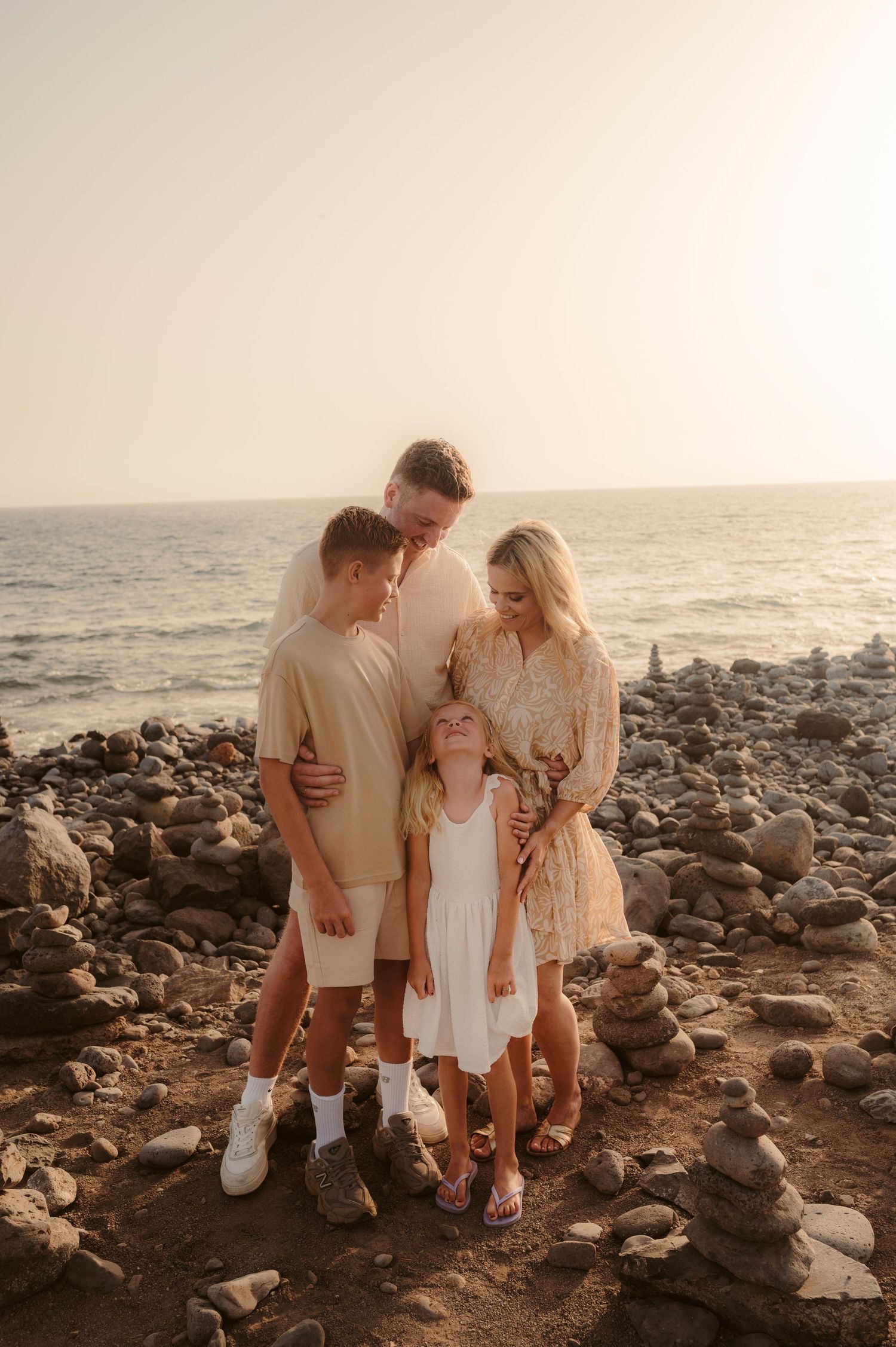 Family portrait with parents and kids looking at each other by sea at sunset, Playa del Duque Tenerife