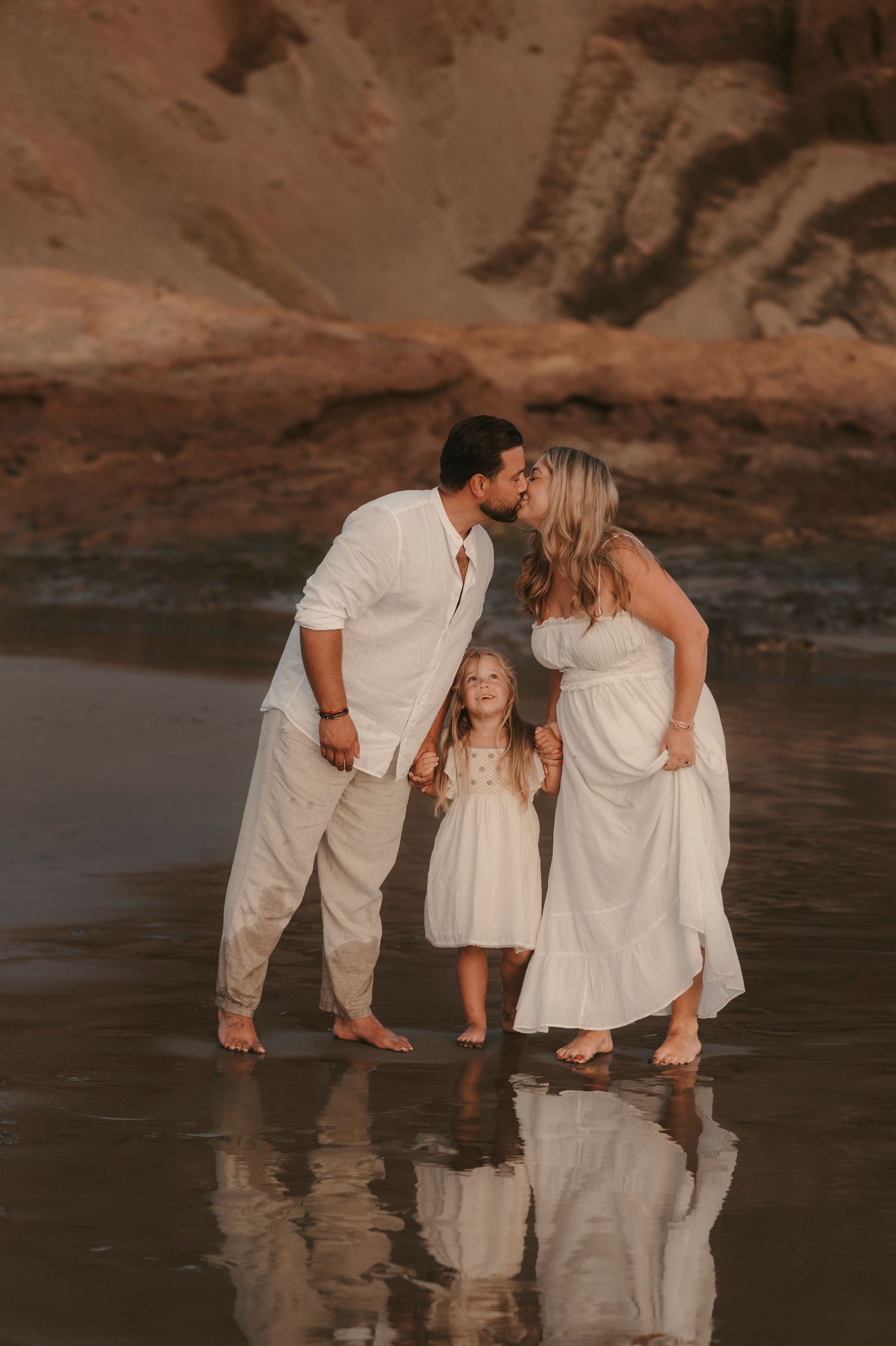 Tender moment captured from afar with parents kissing and little girl admiring them, reflections on the beach at Playa La Tejita
