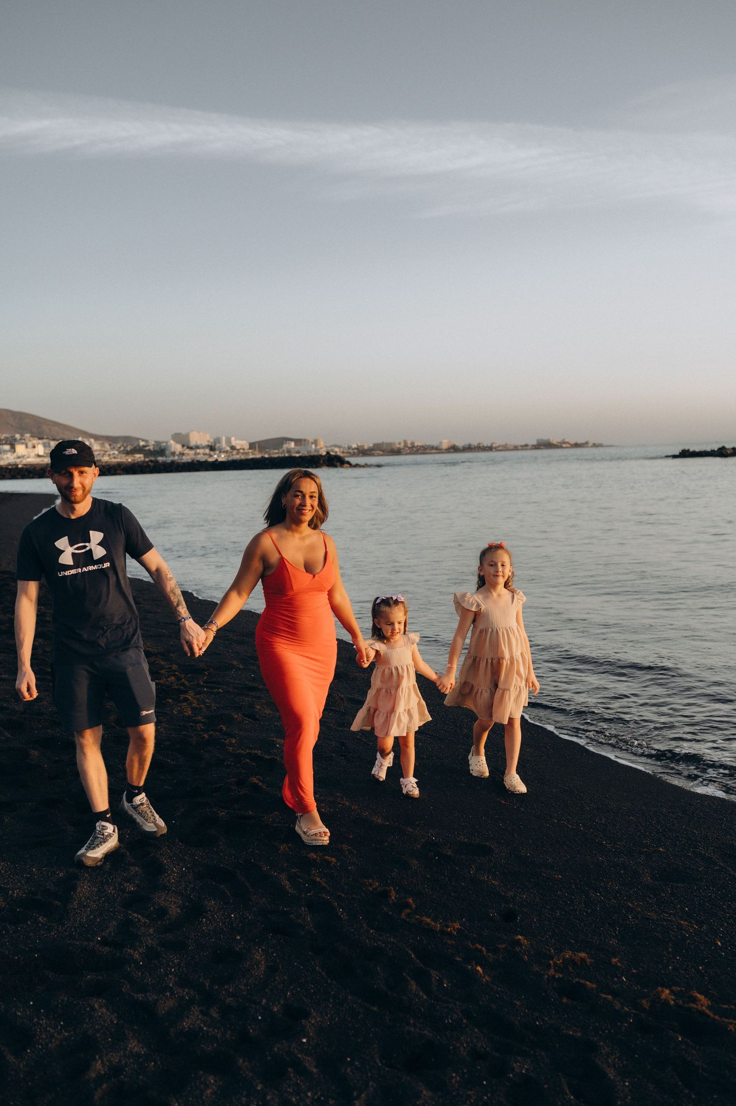 Parents walking with their two daughters during a warm evening on Playa del Duque beach