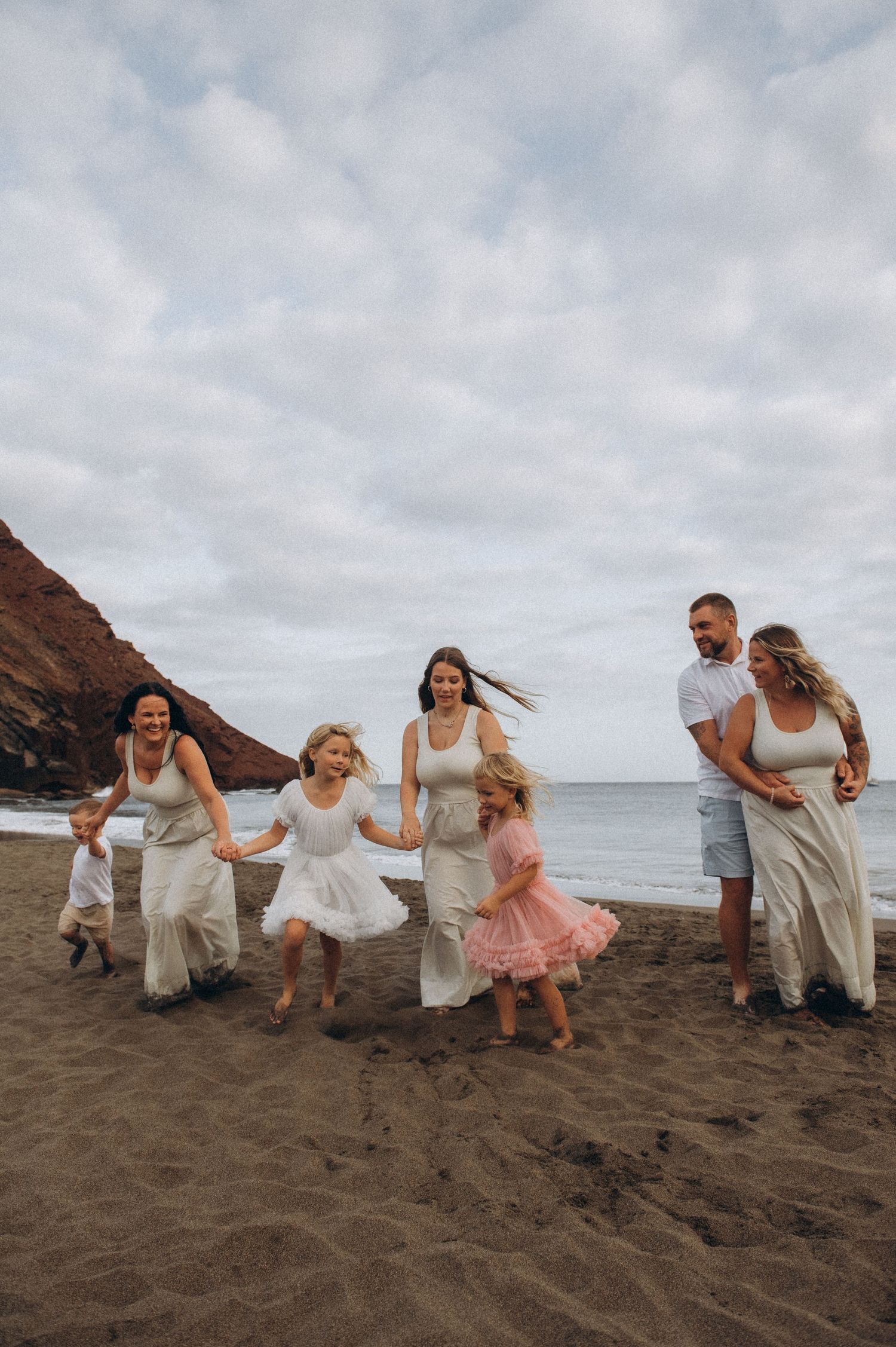 Parents in hug with family gathered around them on beach, Playa La Tejita