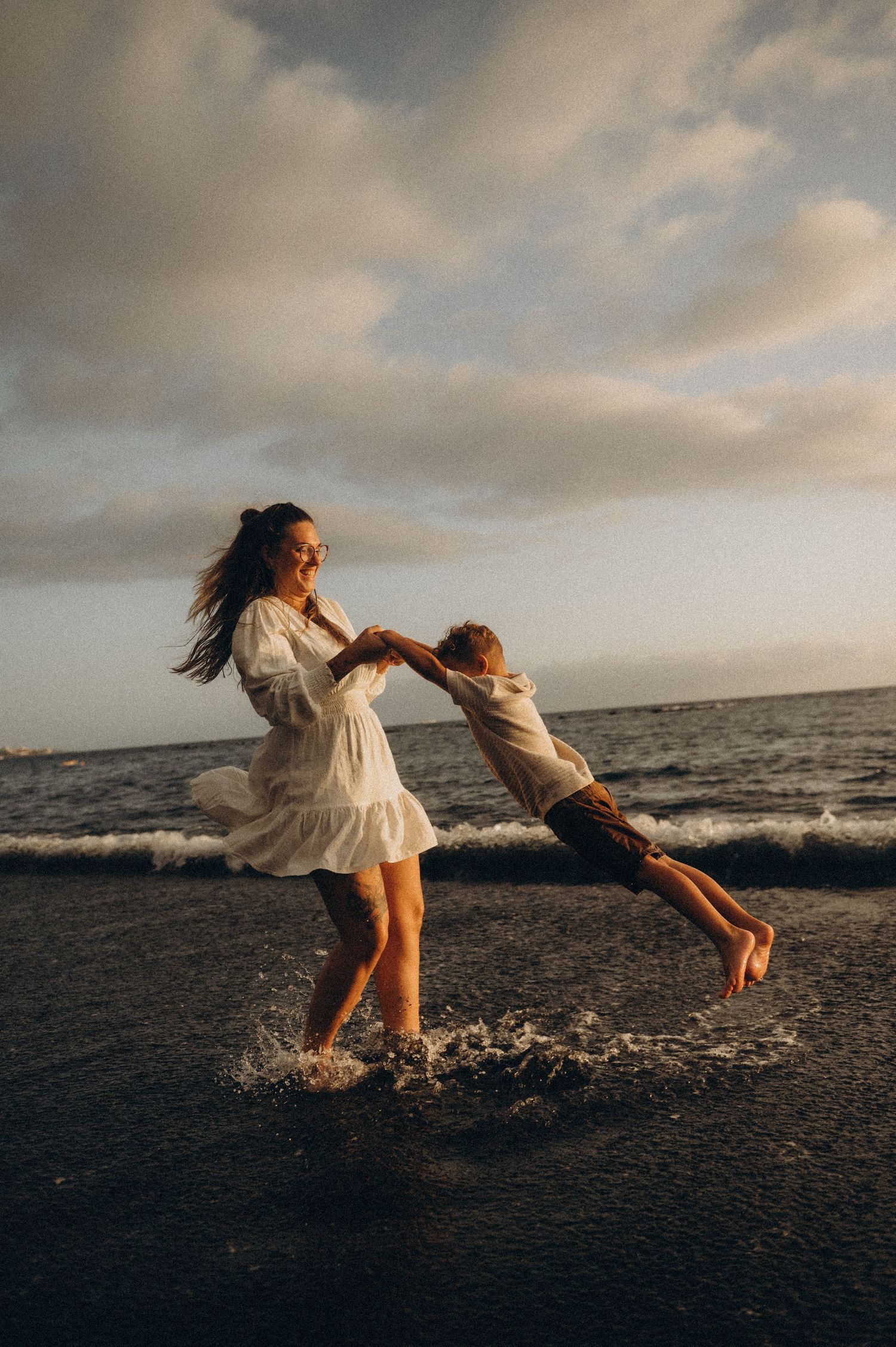 Sunset moment of mom swinging little boy by ocean on Playa del Duque Tenerife