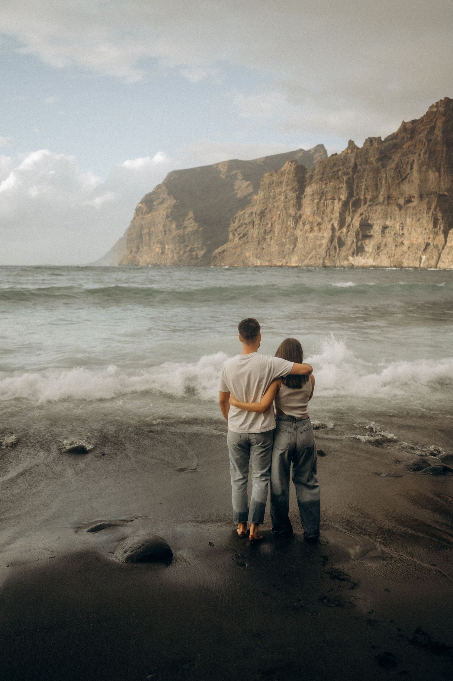 Young couple walking along Playa de Los Guíos beach with Los Gigantes cliffs, Tenerife