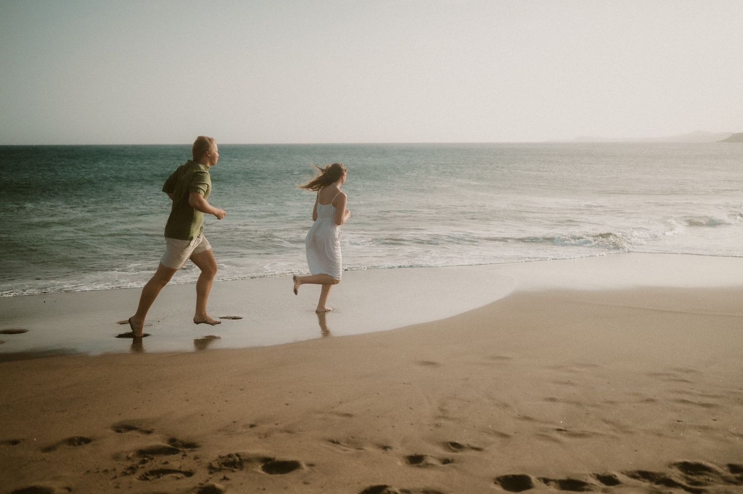 Young couple running barefoot along Playa Tejita beach next to the ocean at sunset, Tenerife couples photoshoot
