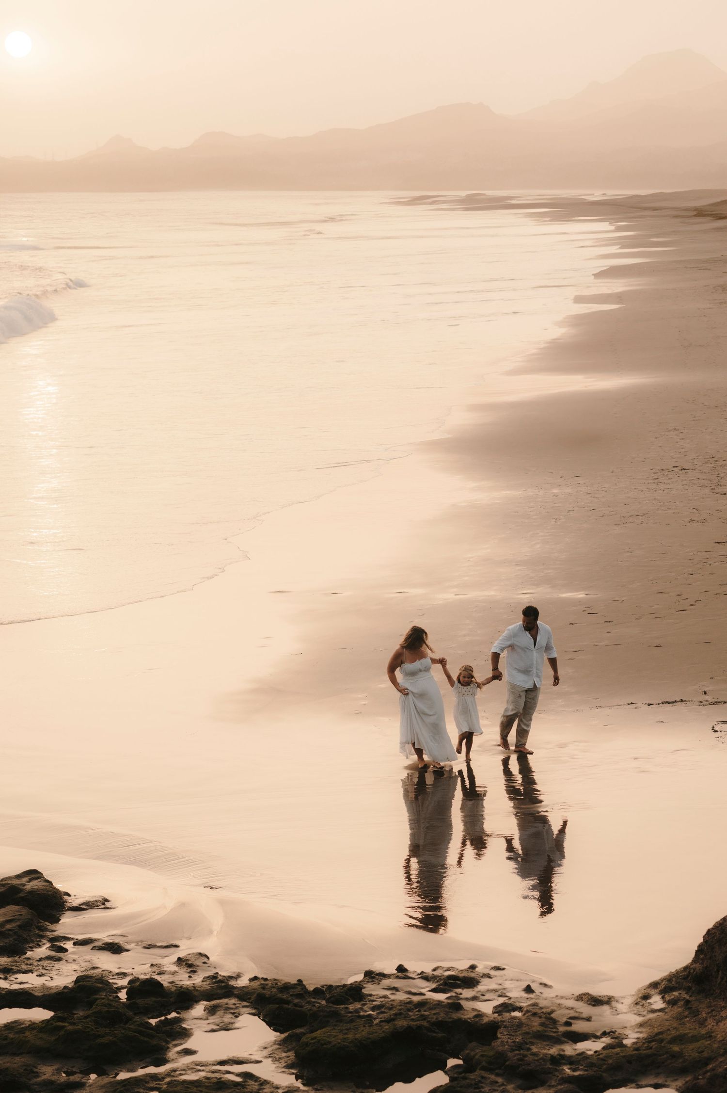 Candid family photoshoot of parents and daughter on Playa de la Tejita, reflections in wet black sand, Tenerife