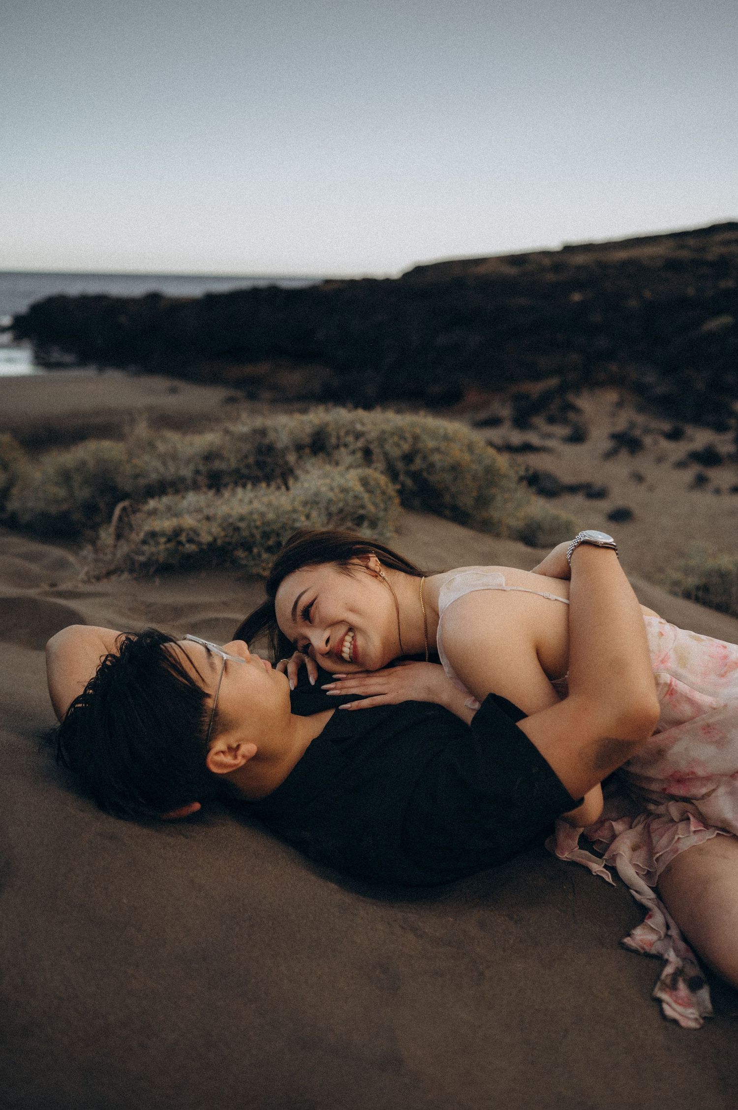 Person in pink dress lying peacefully on dark sand dunes at sunset Montana Pelada beach