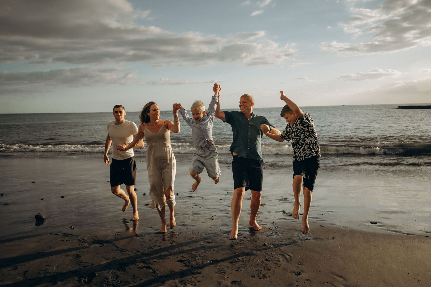 Parents and siblings swinging toddler in air near sea at Playa Fañabé Tenerife