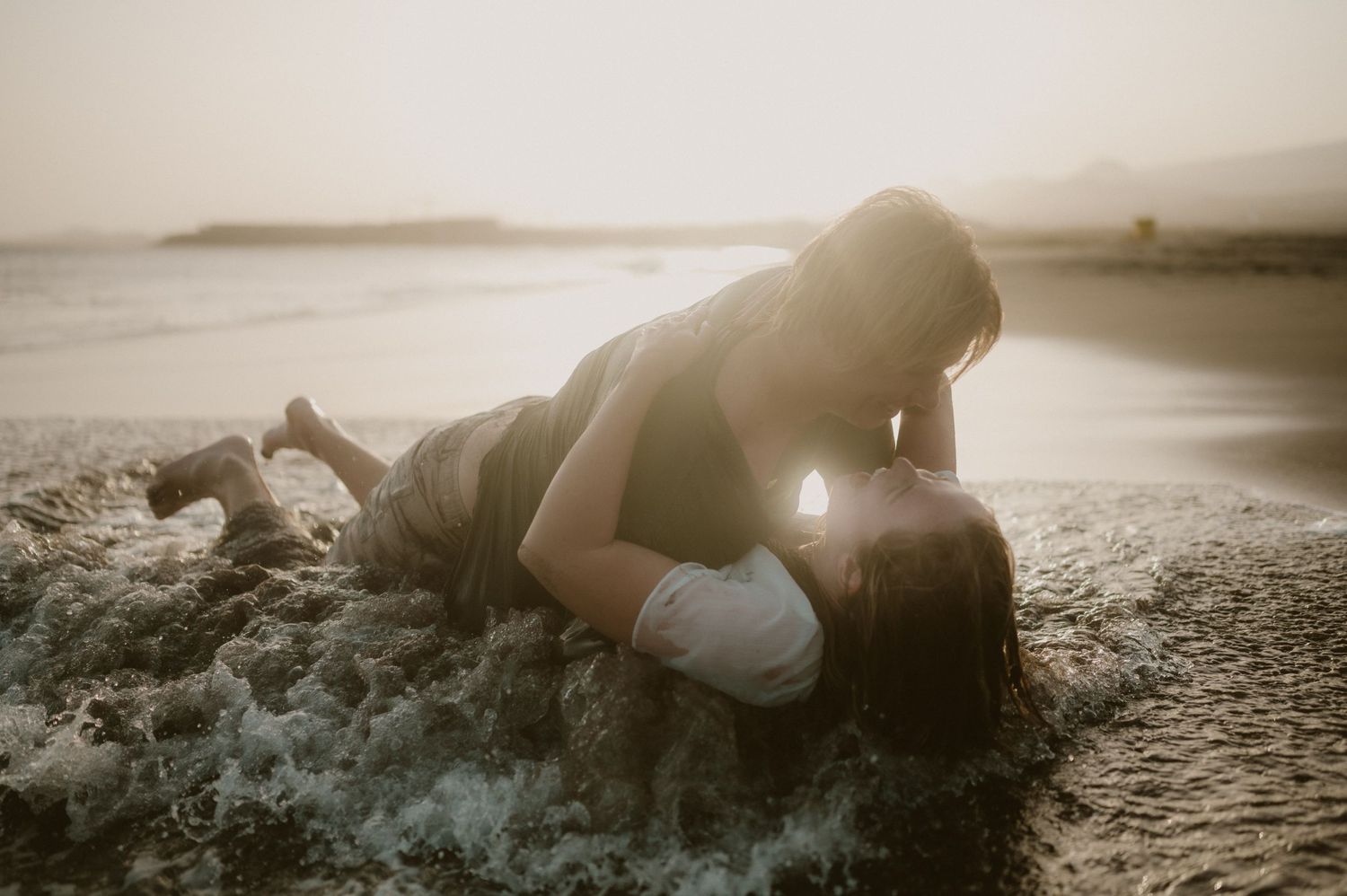 Couple lying in each other’s arms in the ocean waves at Playa Tejita during sunset, Tenerife couples photoshoot