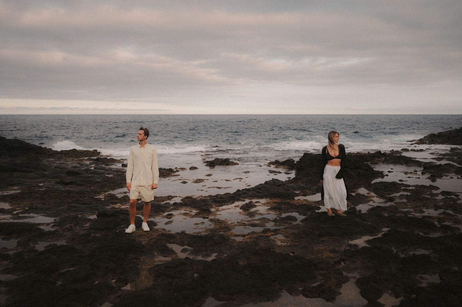 Young couple standing side by side on the rocks with the endless ocean in the background under Montaña Roja, Tenerife