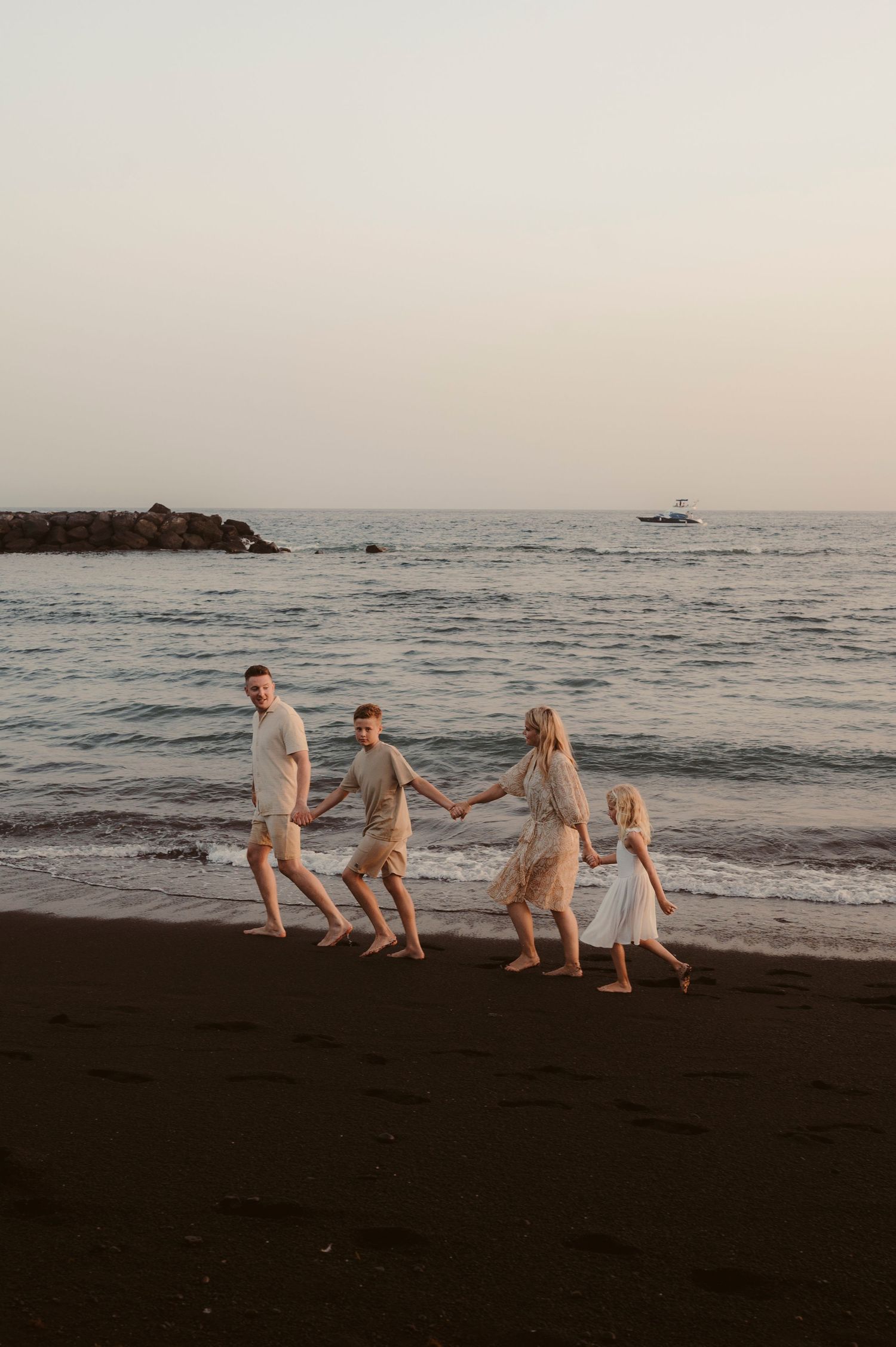 Parents and children strolling from sea onto dark sand.