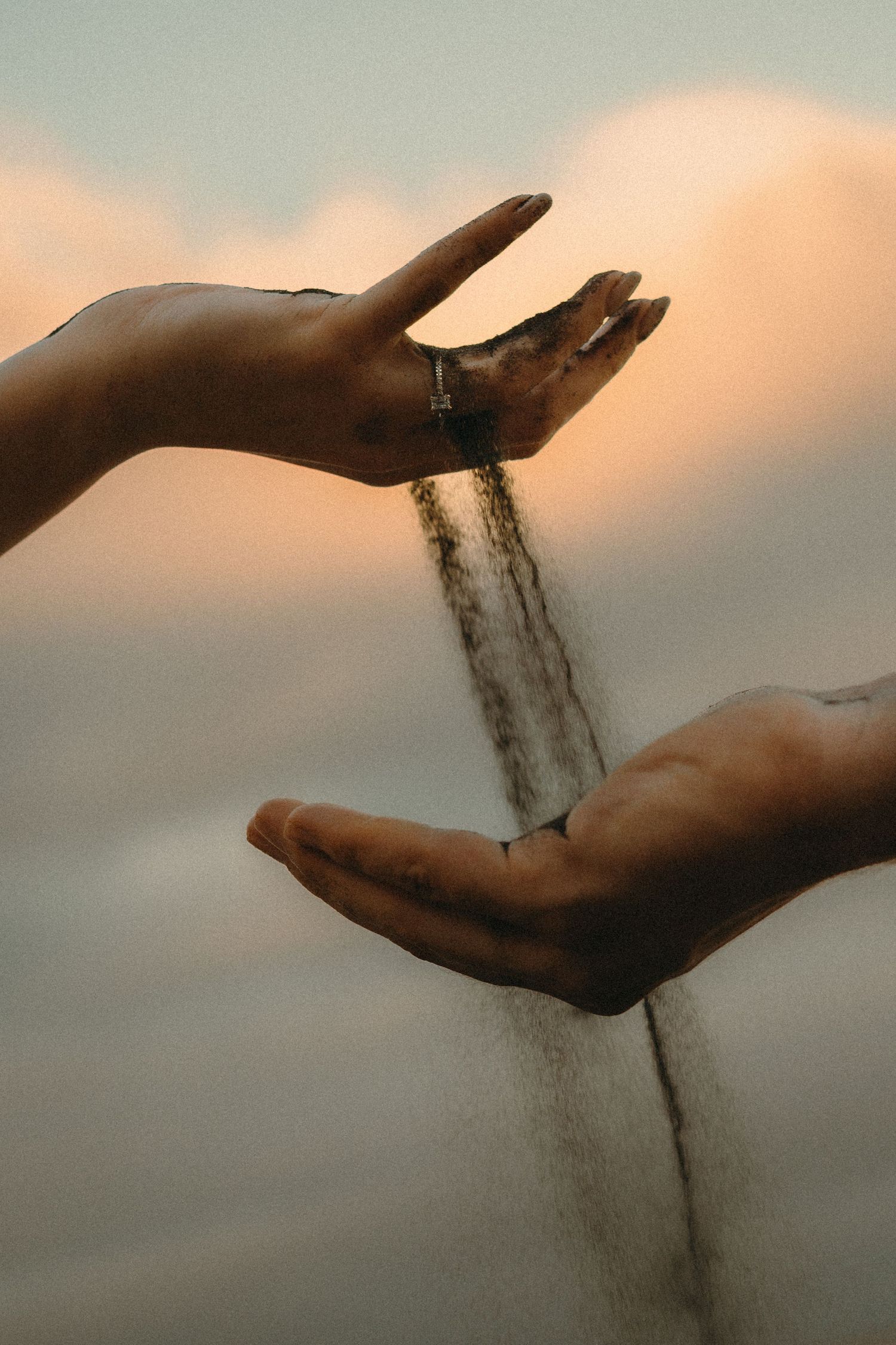 Sand slipping through two hands against a dramatic sunset sky, symbolizing the passage of time.