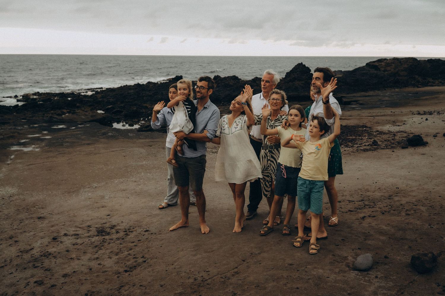 Big family photoshoot with ten people waving to drone by the ocean in Tenerife