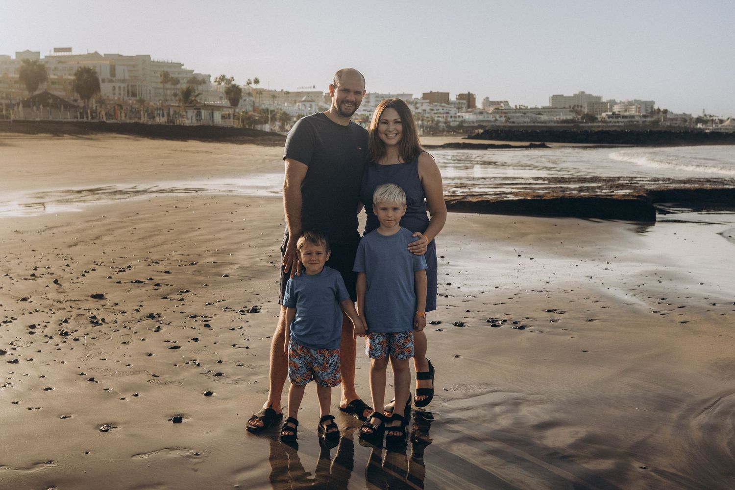 Warm morning moment of a family of four posing on Playa Fañabé’s sandy shore at sunrise, natural family photography