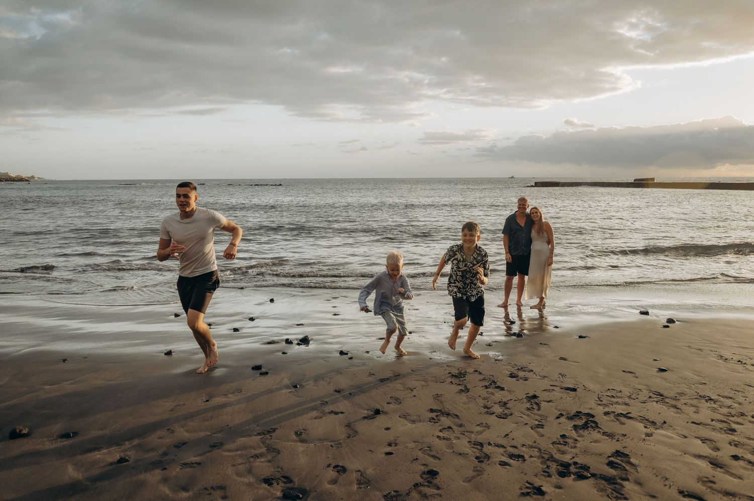 Parents standing in ocean at sunset while sons run along beach, Playa Fañabé Tenerife