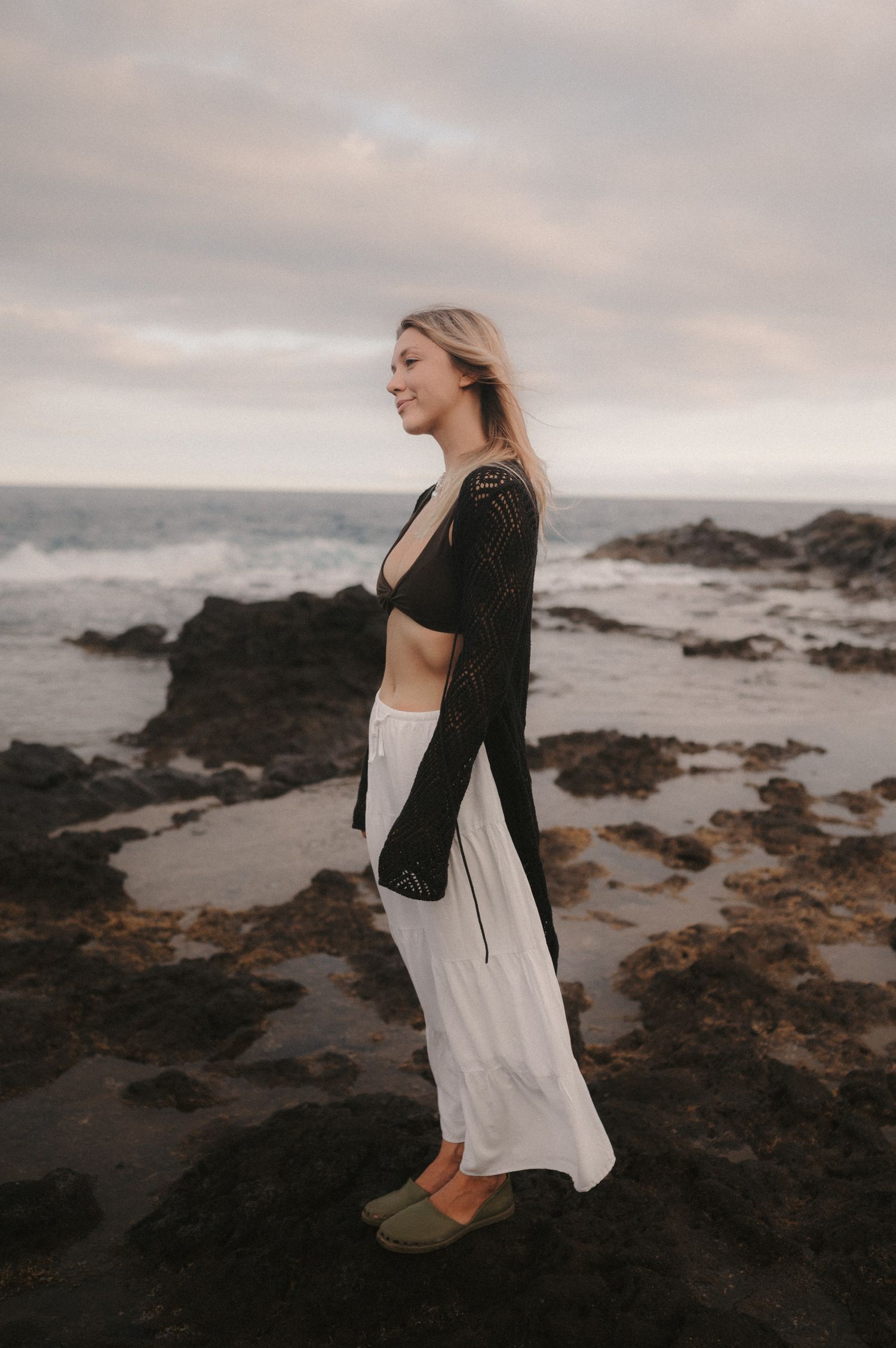 Close-up of a woman from the loving couple, enjoying the moment during a photoshoot on the rocks by the ocean under Montaña Roja, Tenerife