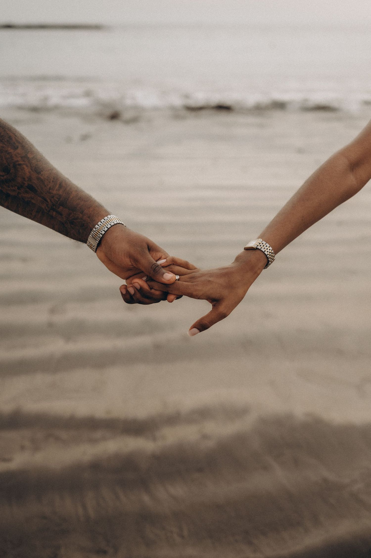 Close-up of couple holding hands with ocean in background