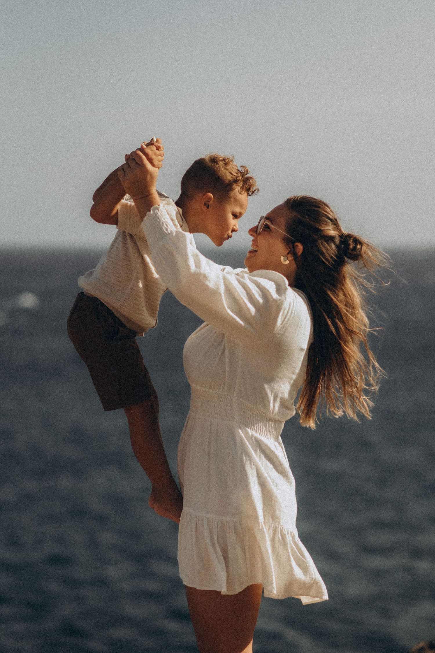 Mother lifting toddler by hands, touching noses and gazing at each other, Playa del Duque
