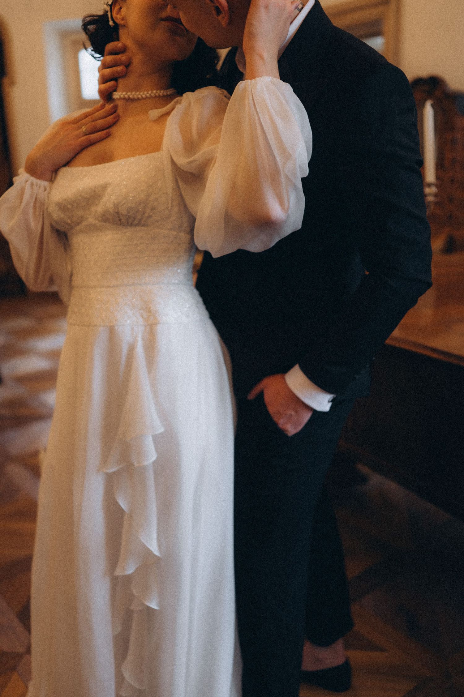 Groom embracing the bride from behind while she gently holds his head during their wedding photoshoot.