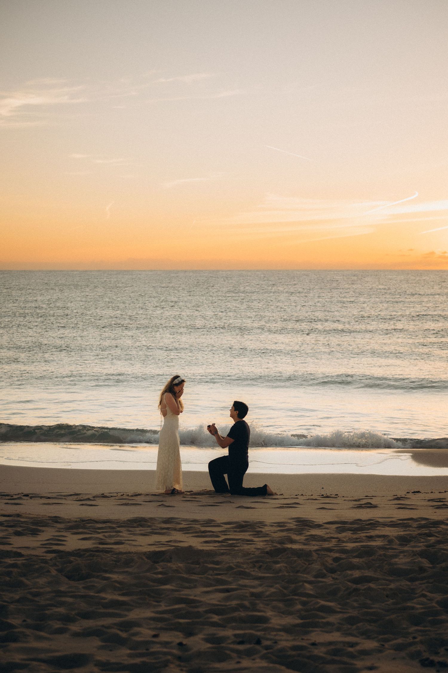 Man proposes to woman on one knee at a romantic beach sunset, with golden ocean horizon in the background.