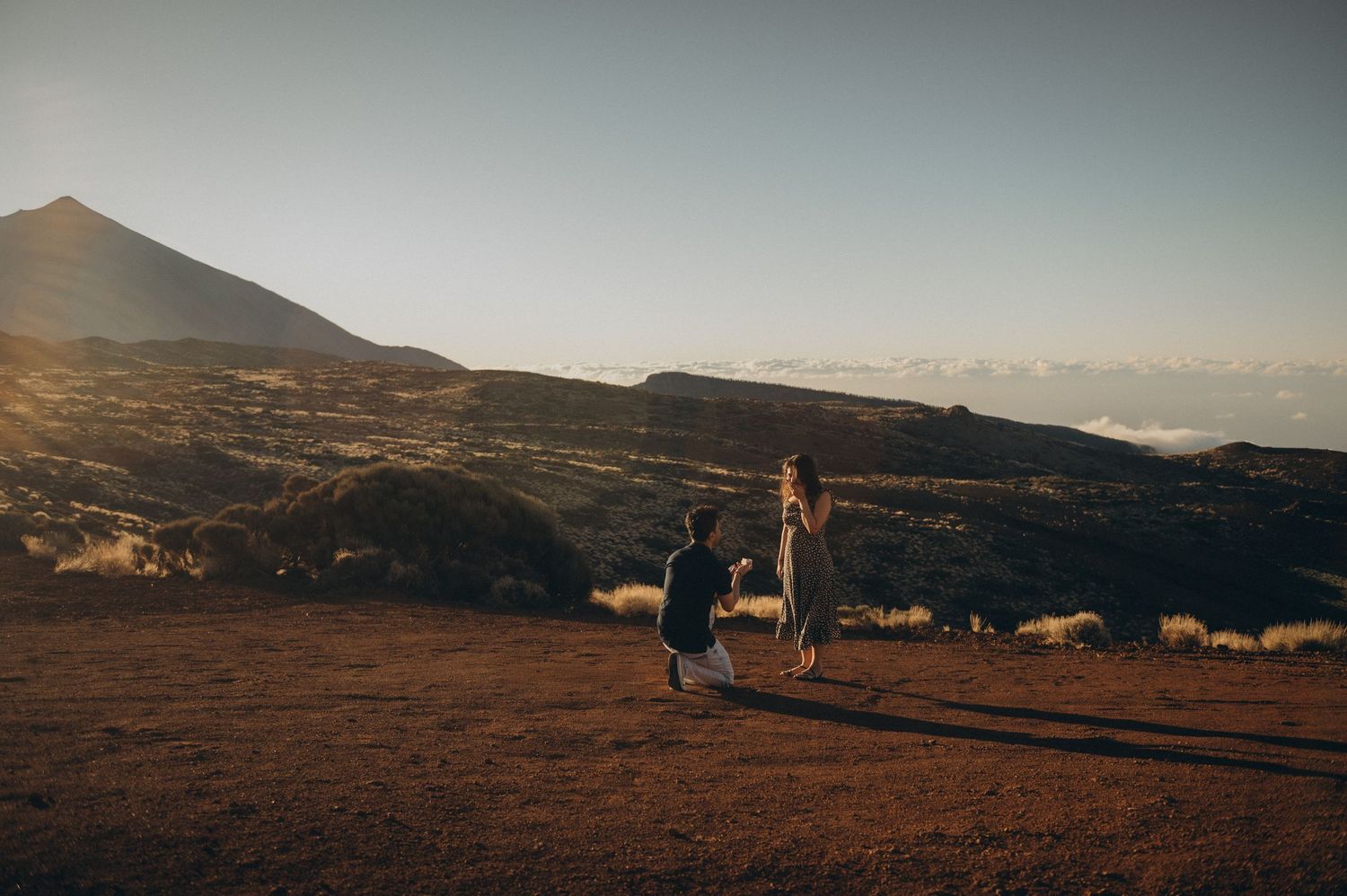 Romantic surprise proposal in Tenerife on a volcanic landscape at sunset with mountain peak in the background.