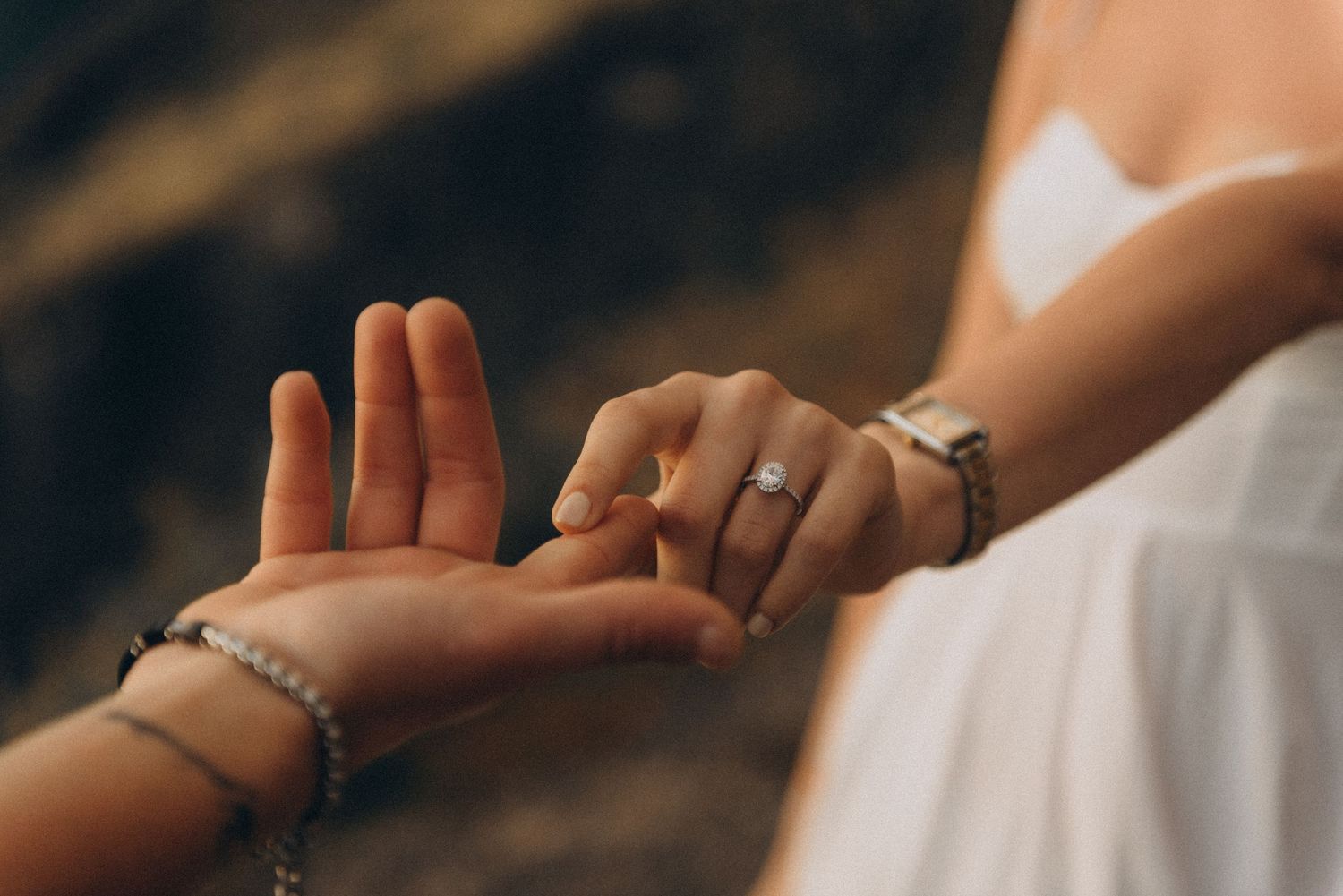 Close-up of two hands touching, one wearing a diamond engagement ring and silver bracelet, the other with a beaded bracelet.