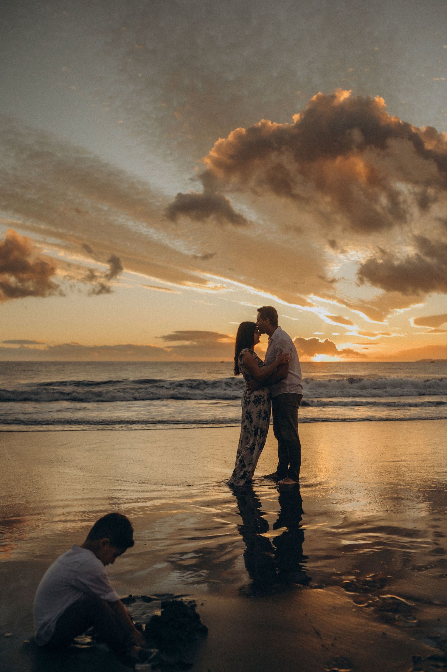 A sunset beach scene with people on wet sand as golden clouds fill the sky above the ocean.