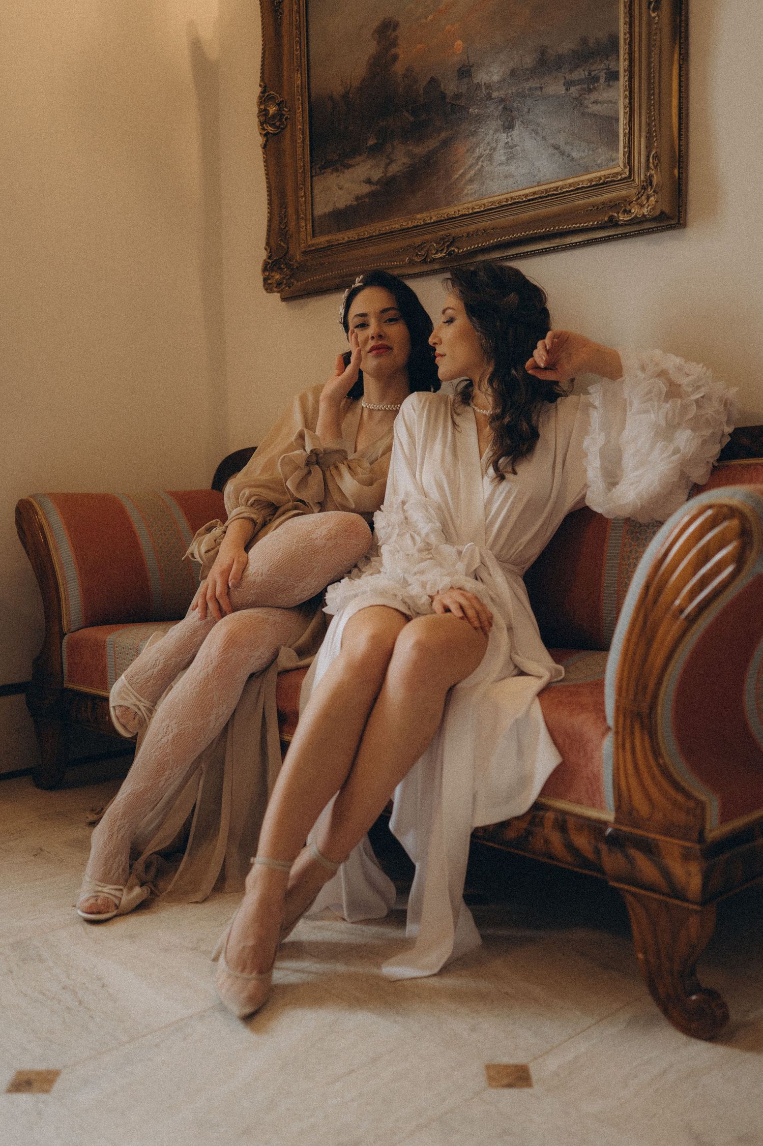 Fine art wedding editorial featuring two brides on a luxurious vintage sofa in a classical castle-inspired setting.