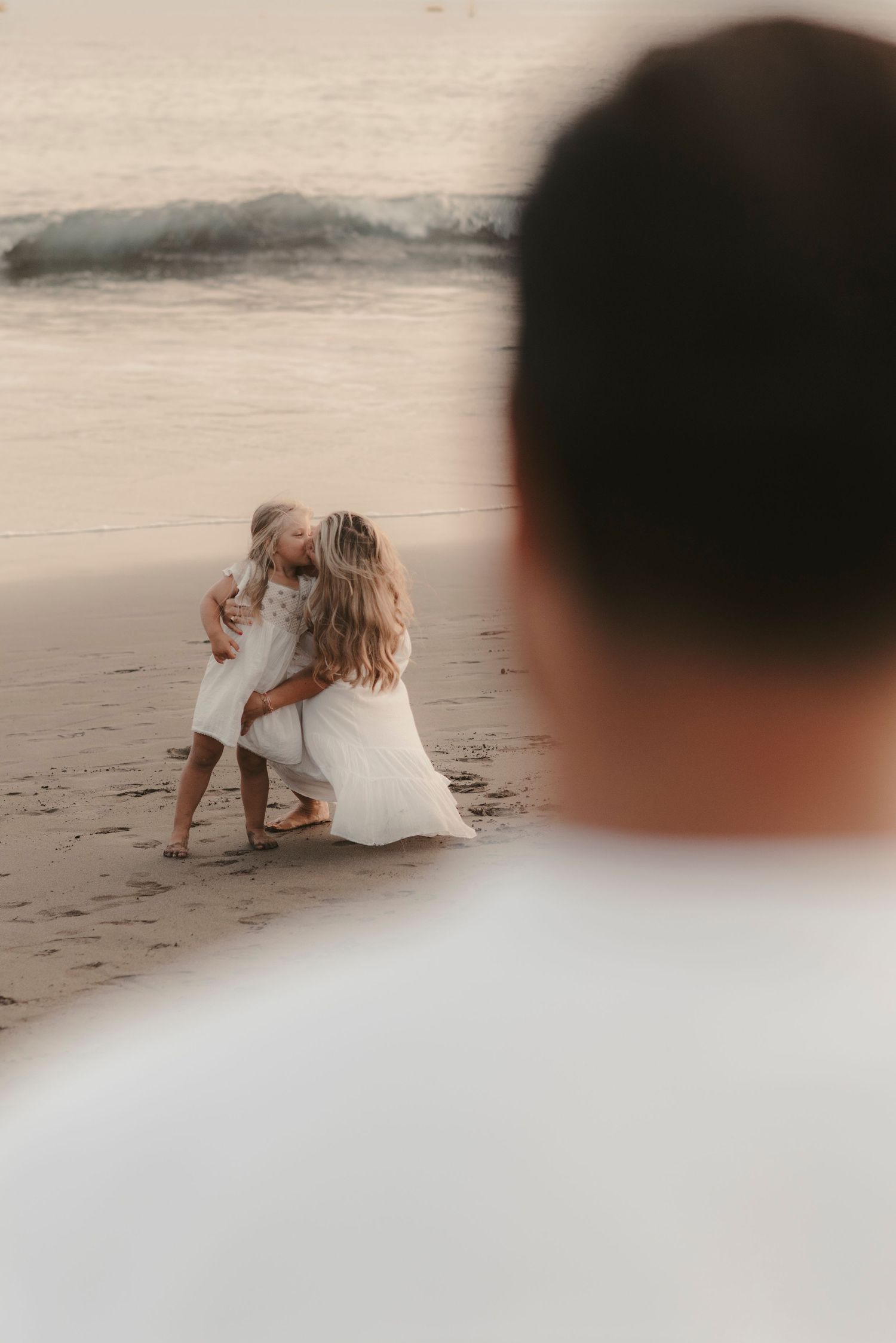 Mother kissing her little daughter while father watches from behind, capturing a tender family moment, Tenerife