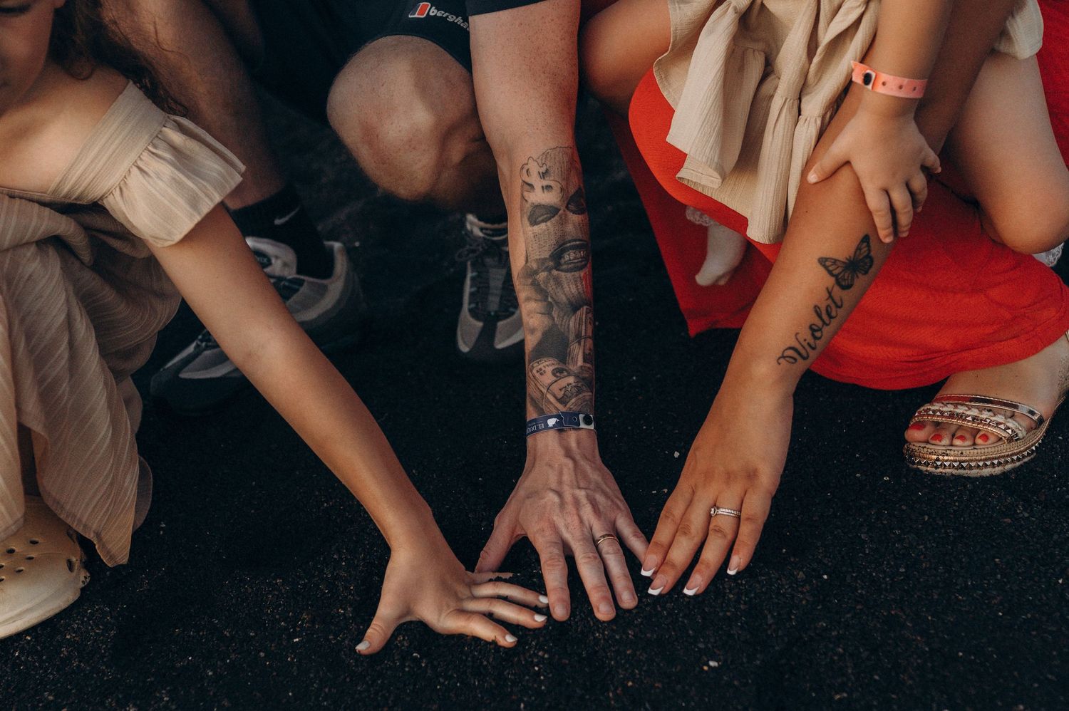 Detail of parents and children hands touching black sand on the volcanic beach of Playa del Duque