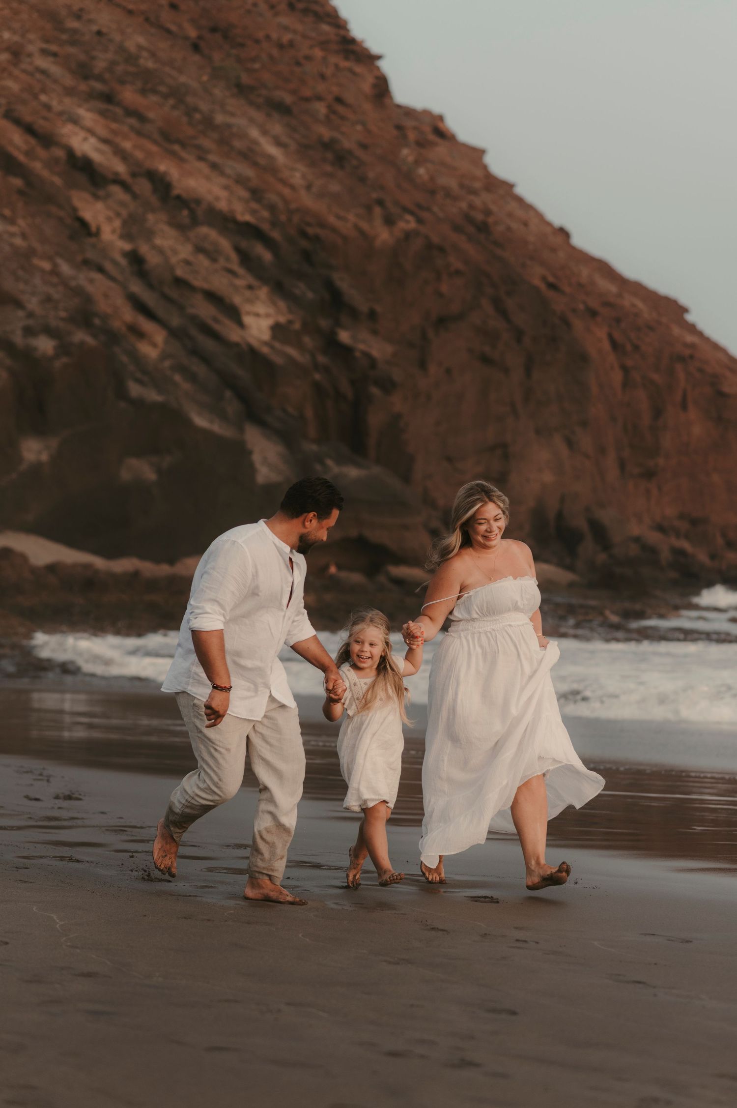 Parents and daughter strolling together on Playa La Tejita with Montaña Roja volcano behind them