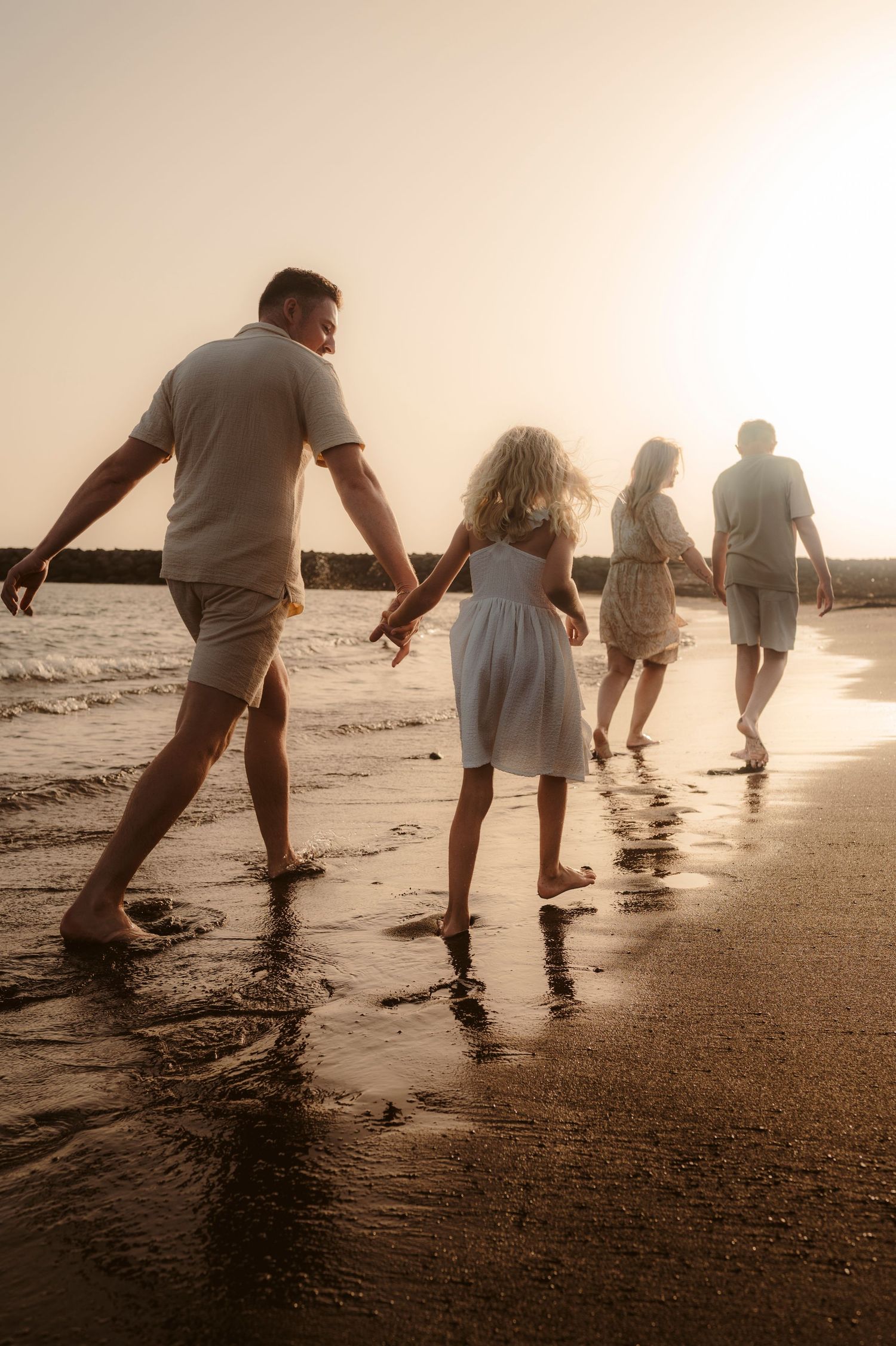 Family walking together along ocean on warm beach at sunset, Playa del Duque