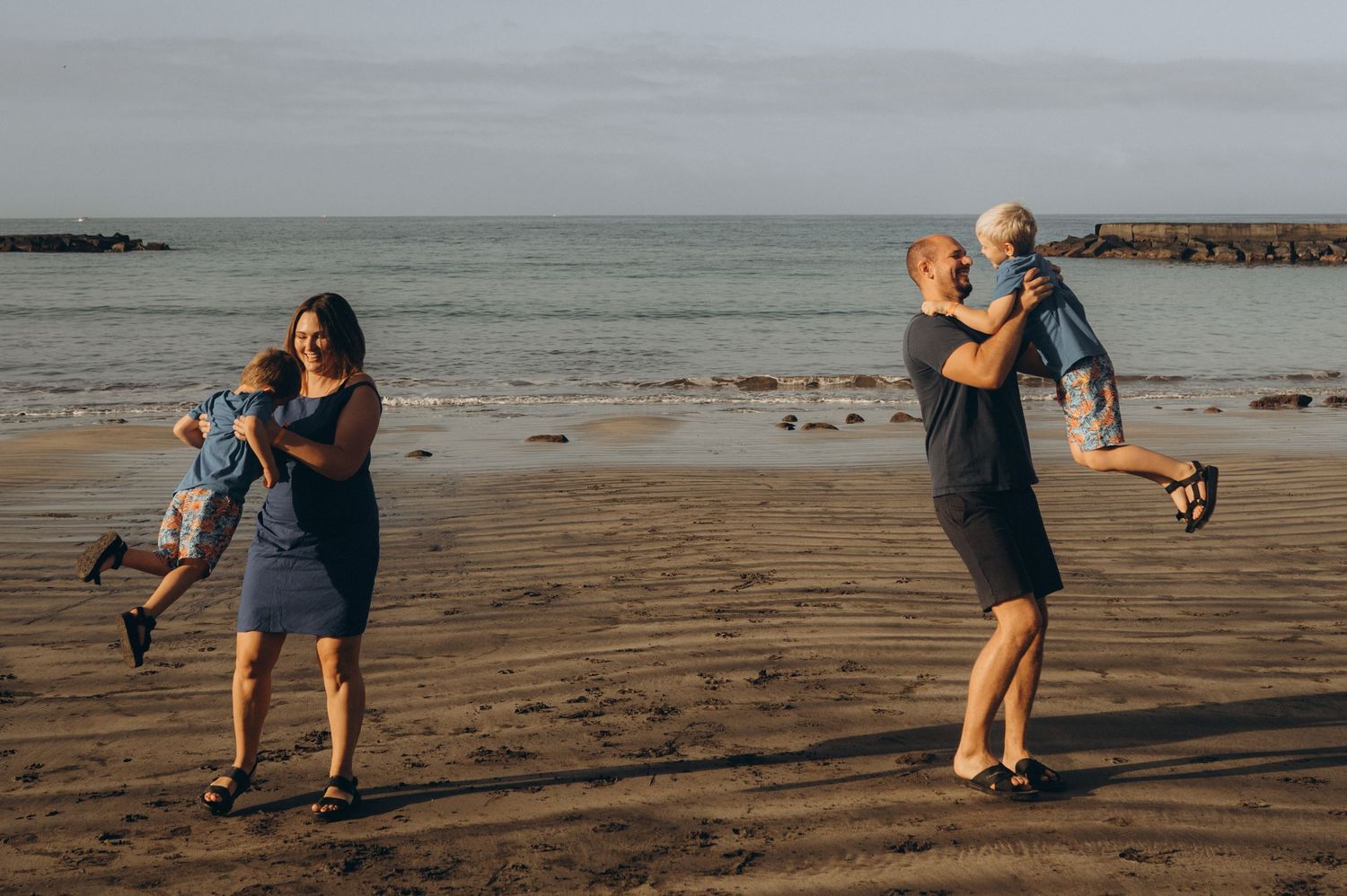 Tender family moment with parents spinning their children in the air, frozen in time by the Atlantic Ocean at Playa Fañabé