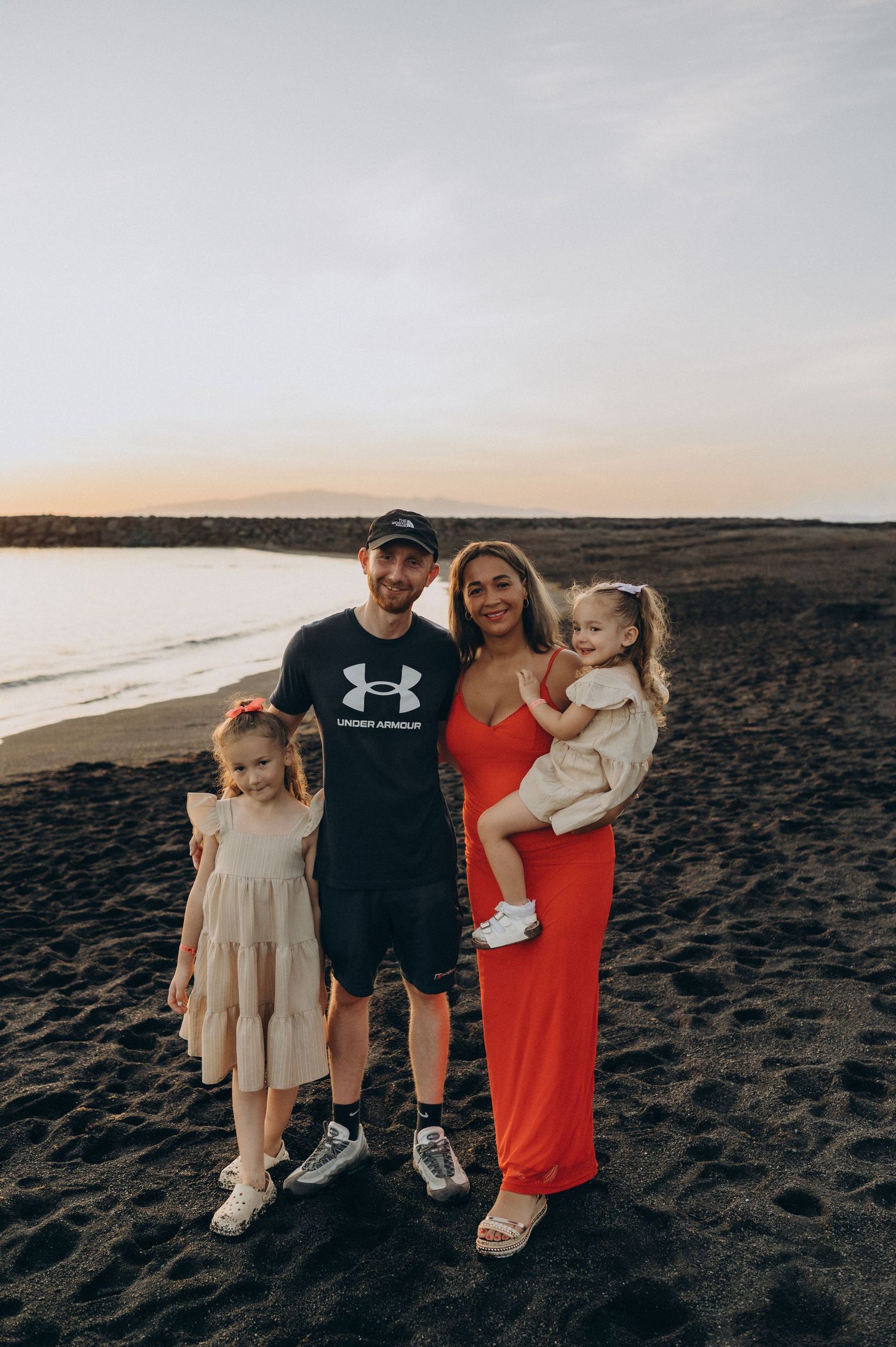 Family posing on a black sand beach at sunset during a family photoshoot in Tenerife
