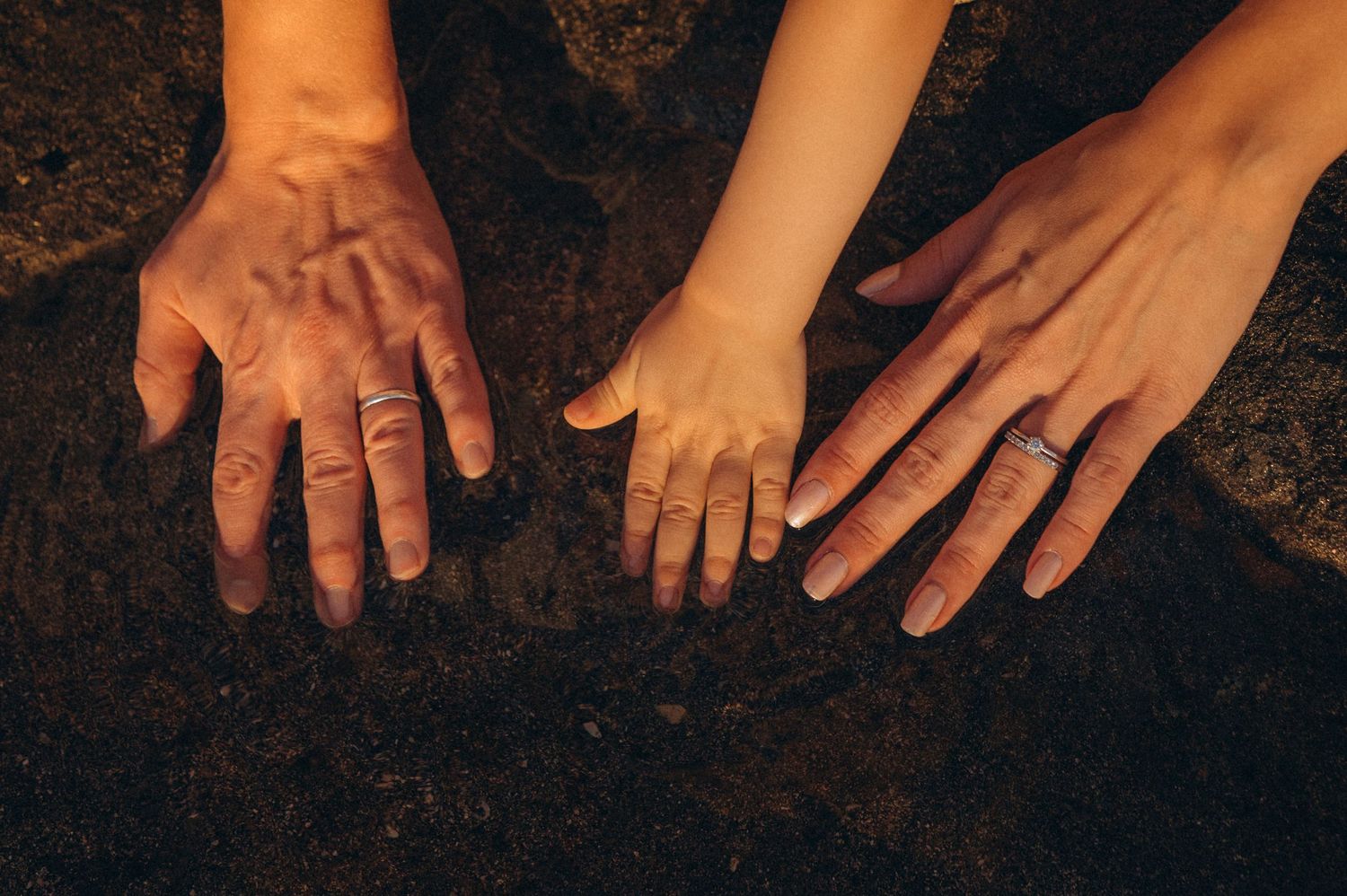 Family detail with little child’s hand between parents’ hands on beach, Las Americas