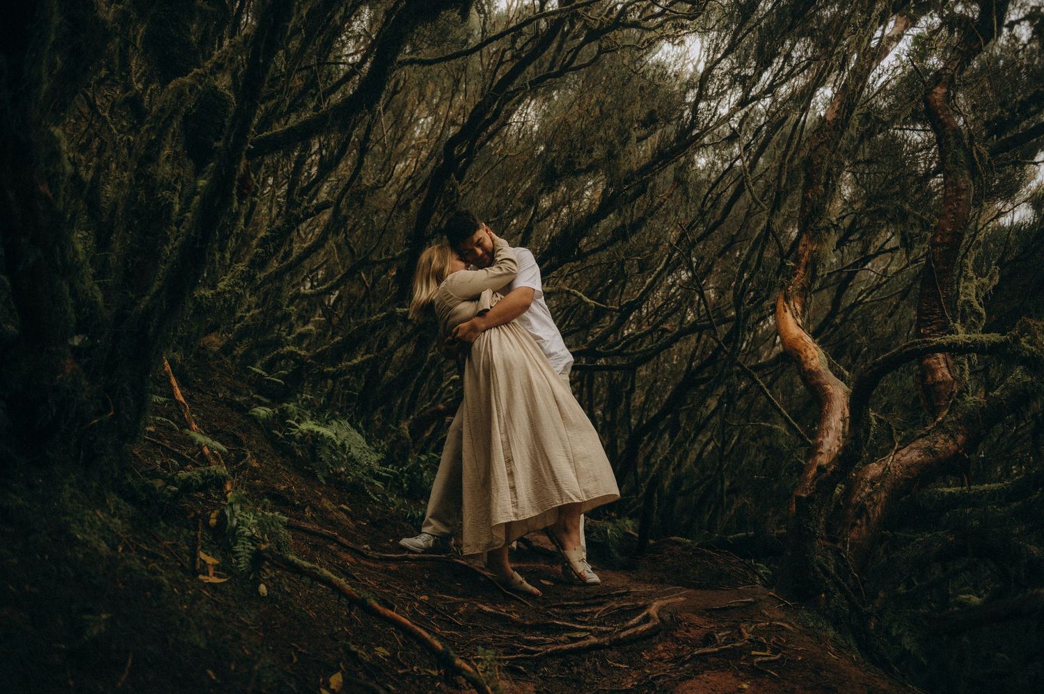 Couple embracing romantically on a mossy forest path surrounded by dark twisted tree, Anaga Park Tenerife