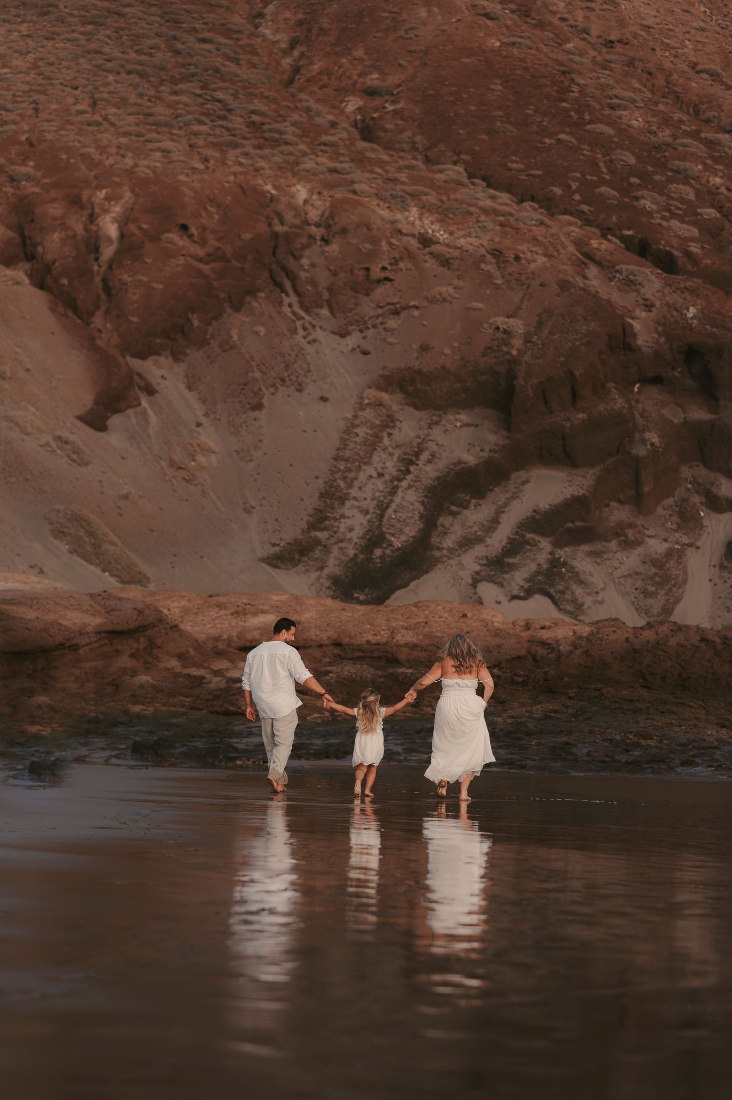 arents and their little daughter enjoying time together on the beach with mirrored reflections in the sand, Tejita