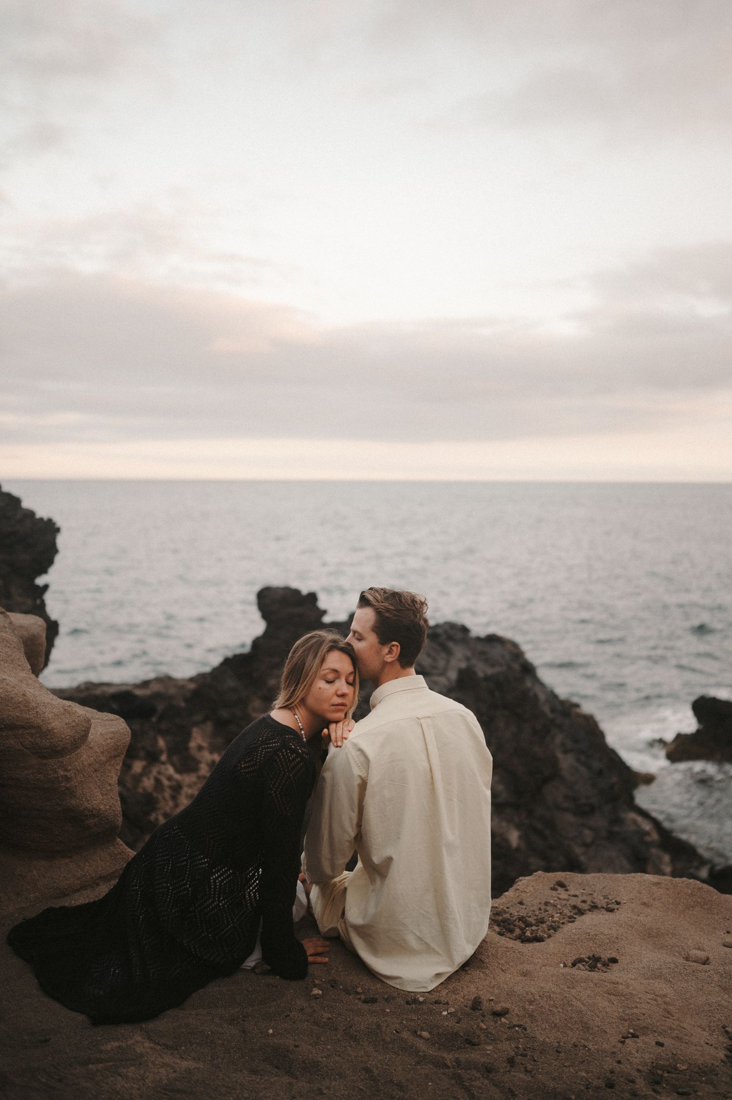Young couple sitting on a cliff with ocean view, enjoying a romantic photoshoot moment in Tenerife