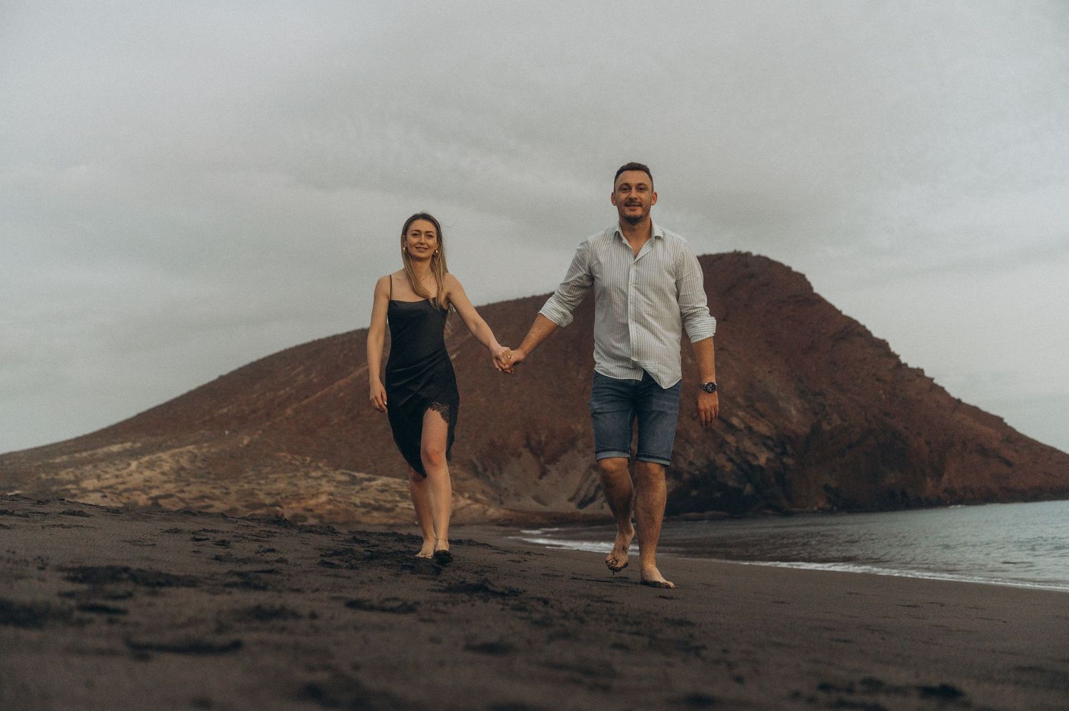 Young couple holding hands and enjoying sunset by Montaña Roja on Playa de La Tejita, Tenerife