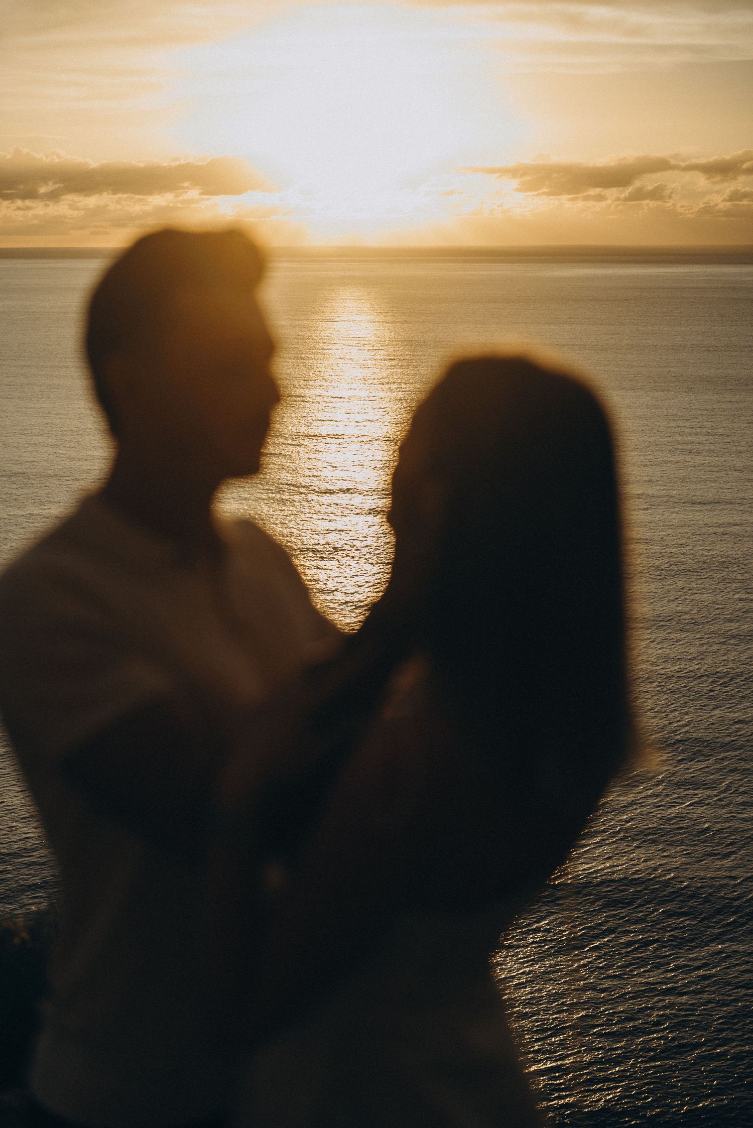 Silhouette of a romantic couple embracing at sunset over the ocean, with golden light reflecting on calm waters.