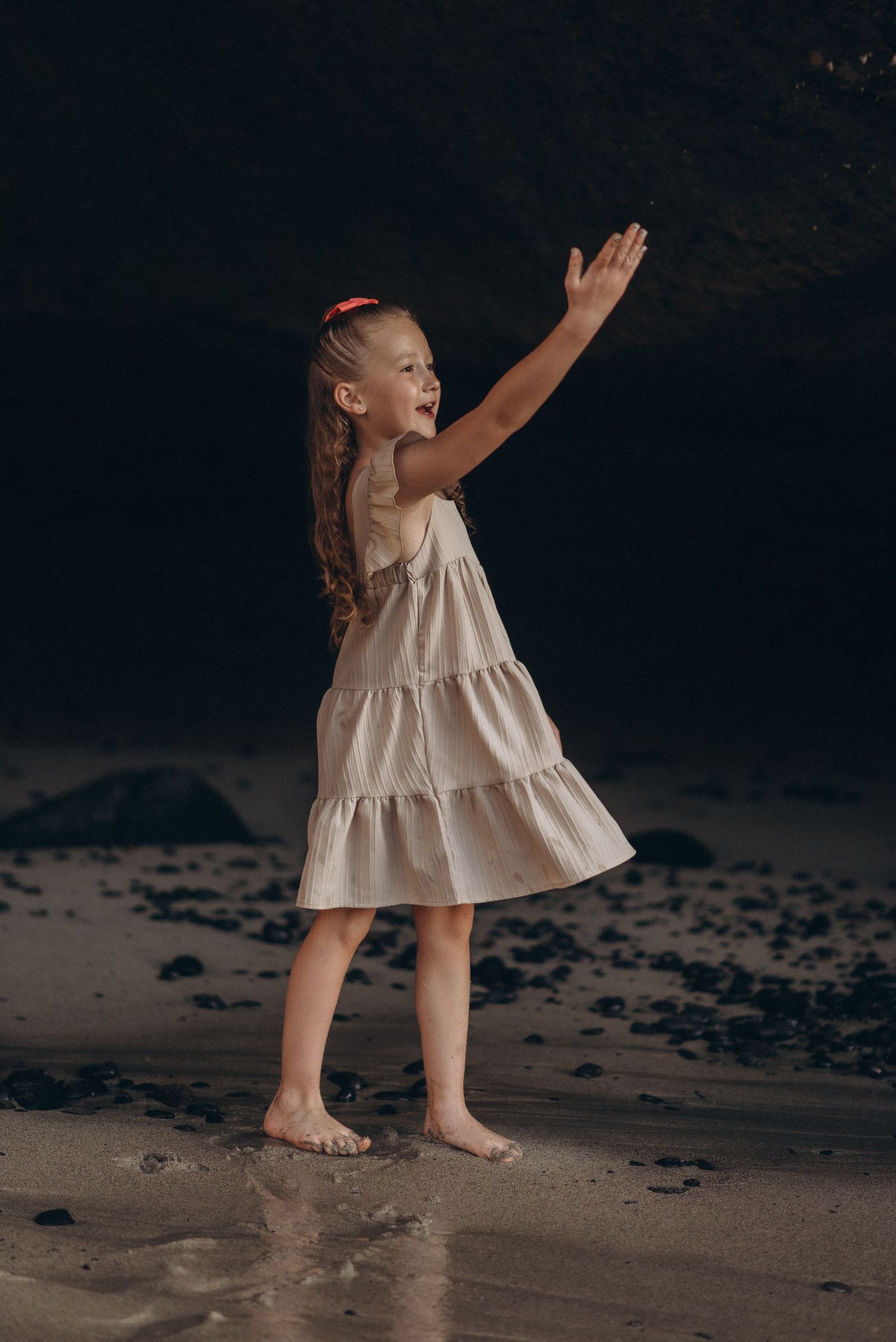 Child playing by throwing pebbles into the waves on a Tenerife beach from distance