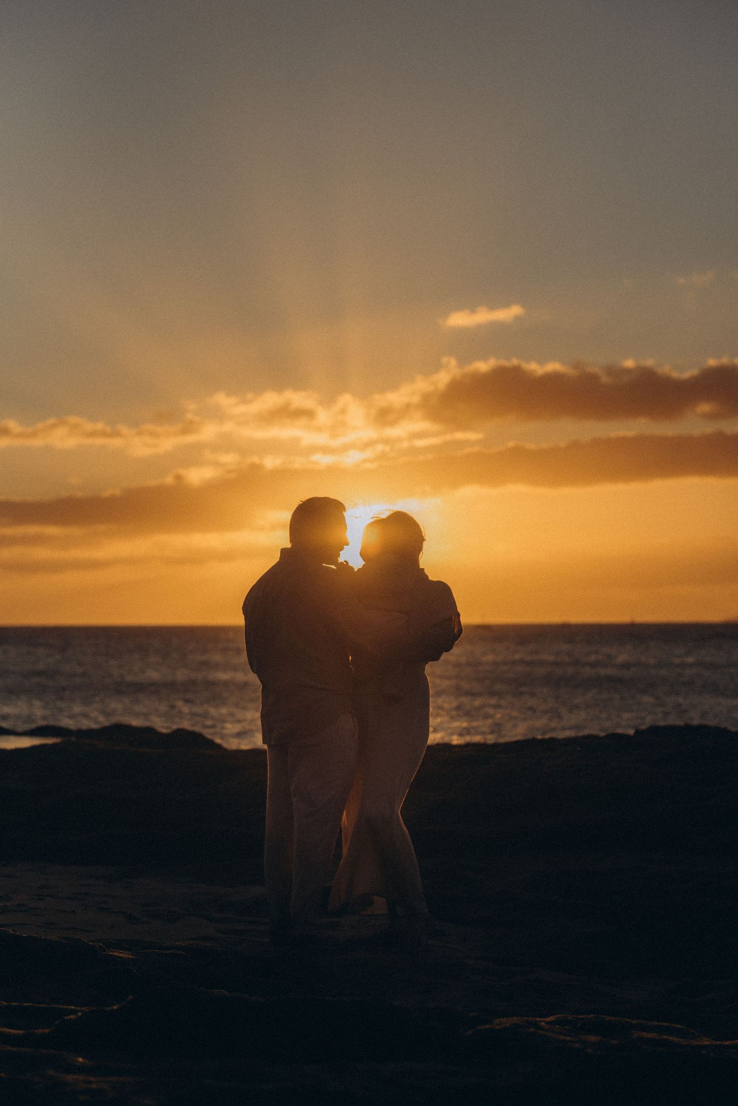 Silhouettes of people embracing against a dramatic orange sunset over the ocean.