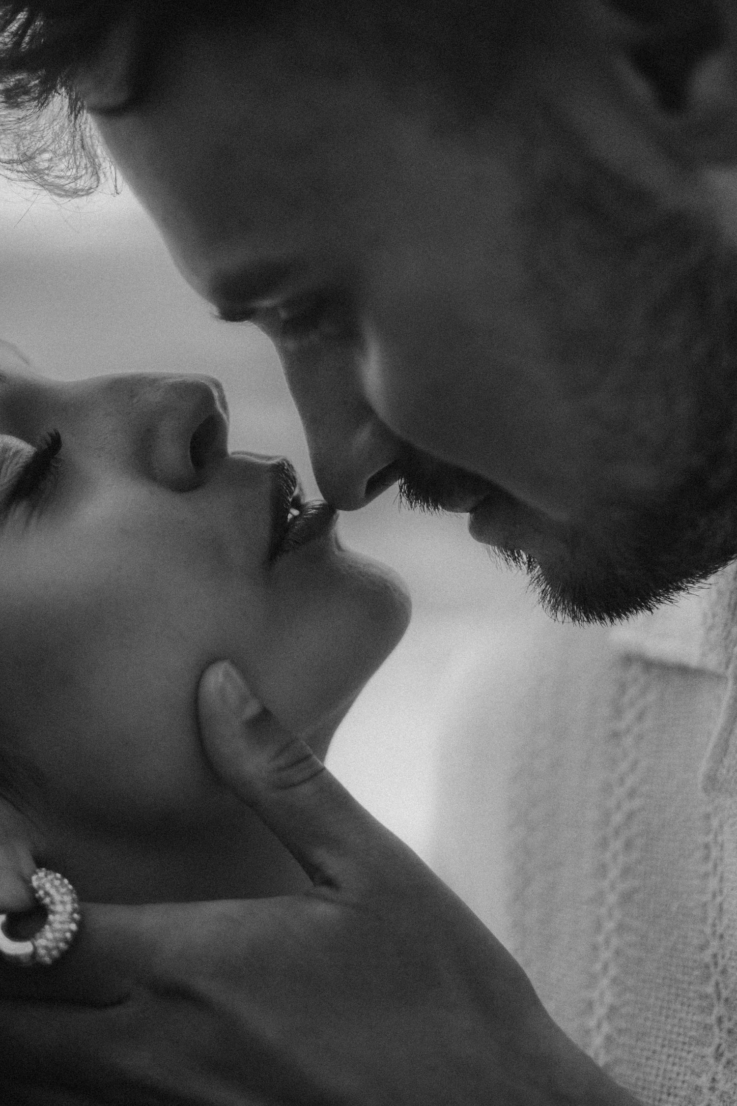 Black and white close-up of a romantic couple sharing a tender kiss, woman wearing pearl earrings.
