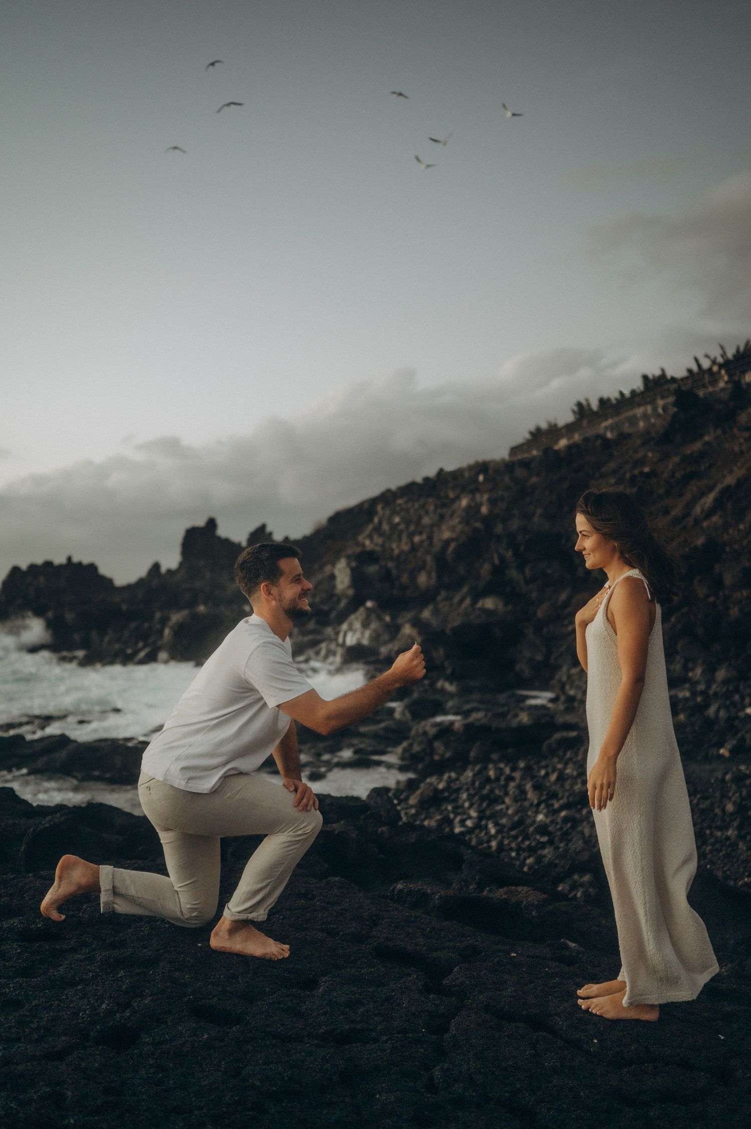Romantic surprise proposal in Tenerife on a rocky coastal cliff at sunset with ocean views.